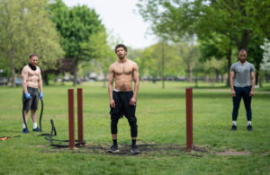 Photograph of 3 men in a park facing the camera mid-exercise regime