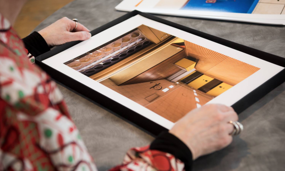 Photograph taken from behind and to the right of a person holding a framed print of a photograph of an interior on a table, during a portfolio review.