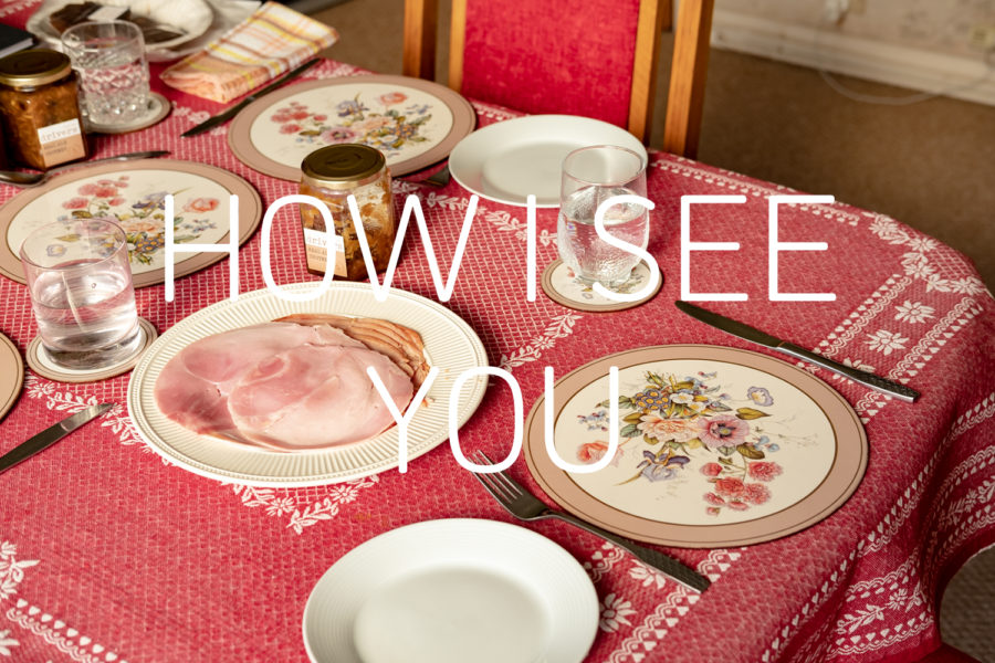 Graphic with a photograph of a table set for lunch with a pink tablecloth, plate of ham, a floral placemat, cutlery, a jar of chutney and glasses of water. Text in white in the middle says 'HOW I SEE YOU'