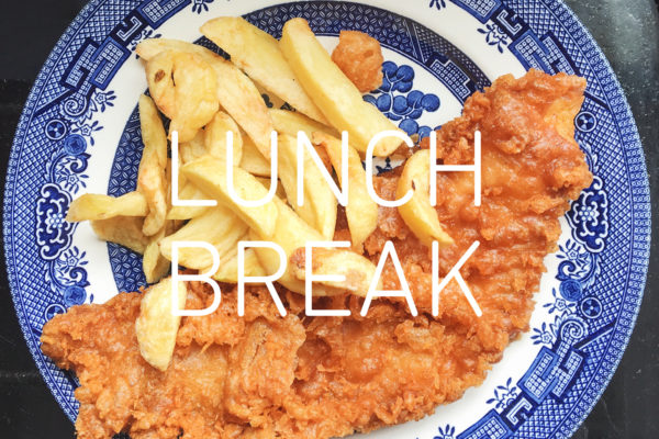 Photograph of a blue and white 'Willow' pattern plate with fish and chips on top, and text reading 'Lunch Break' in white in the centre