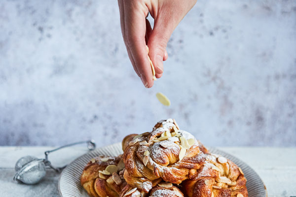 Swedish buns on a plate, with a hand sprinkling chopped almonds from above