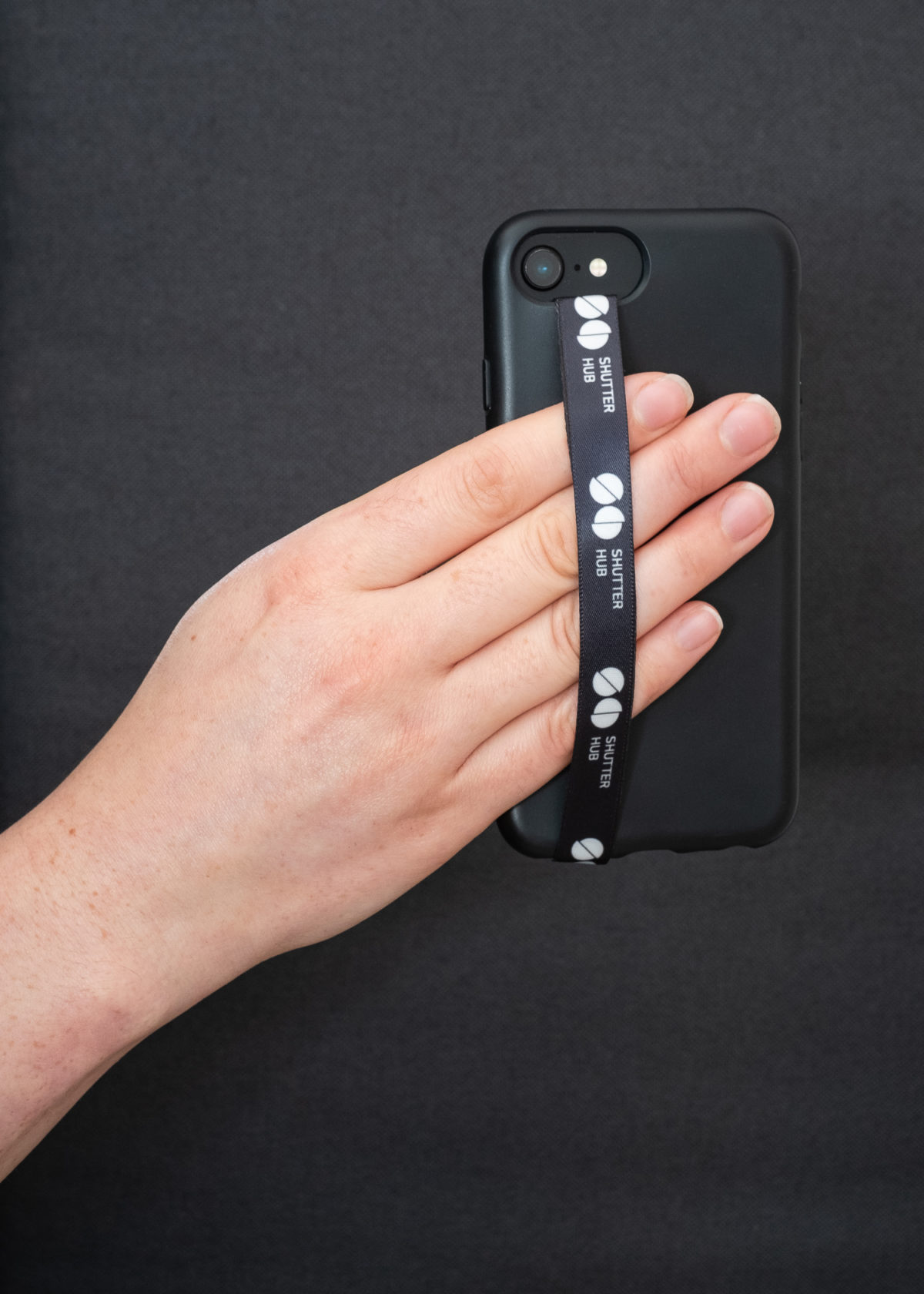 Hand holding a Shutter Hub Phone Loop attached to a black phone case, with the Shutter Hub logo