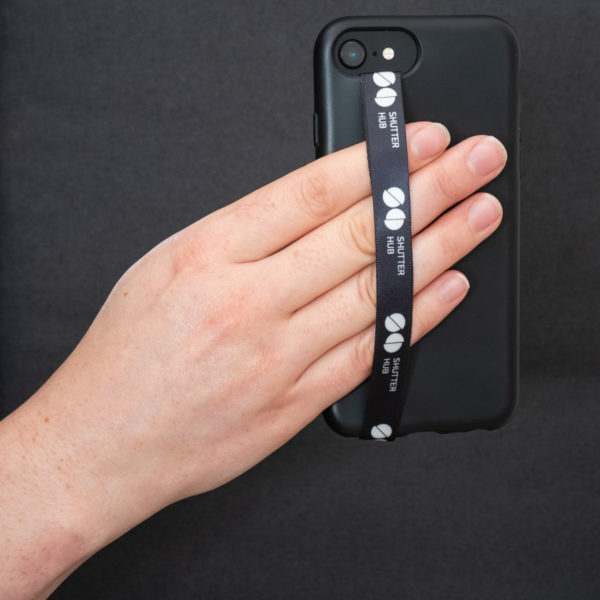 Hand holding a Shutter Hub Phone Loop attached to a black phone case, with the Shutter Hub logo