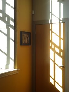 Shadows and reflections of sunshine coming through a barely visible window, casting shadows of glazing bars against the wall.