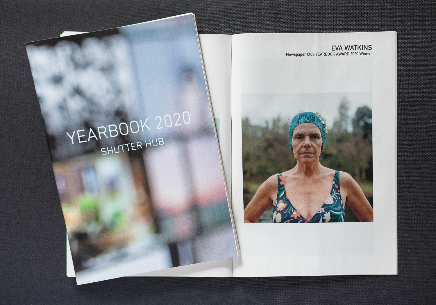YEARBOOK 2020, one copy to the left showing the front cover with out of focus image and 'YEARBOOK 2020, Shutter Hub' in text, and an open copy underneath, opened to show 'EVA WATKINS, Newspaper Club YEARBOOK 2020 Award Winner' and an image of a synchronised swimmer