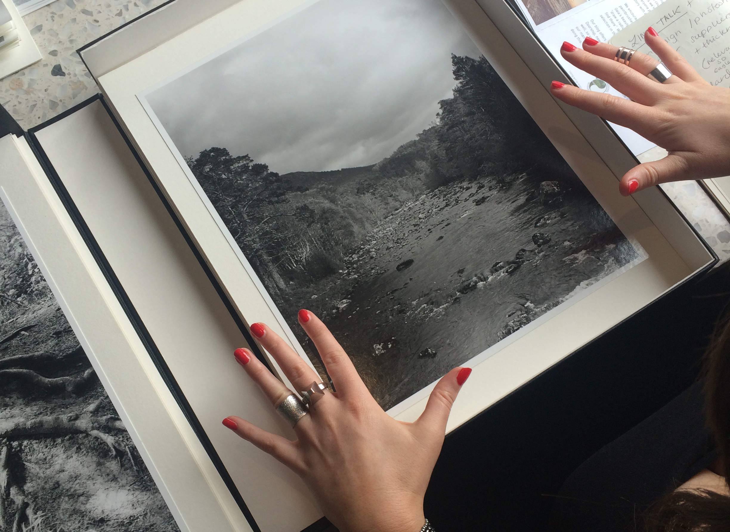 Hands with red painted nails and ornate rings either side of a box with a black and white photograph