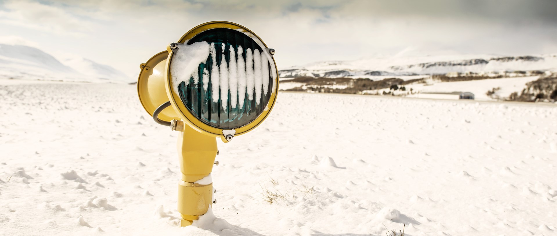 Snow-covered airport runway light near Akureyri with winter hills beyond.