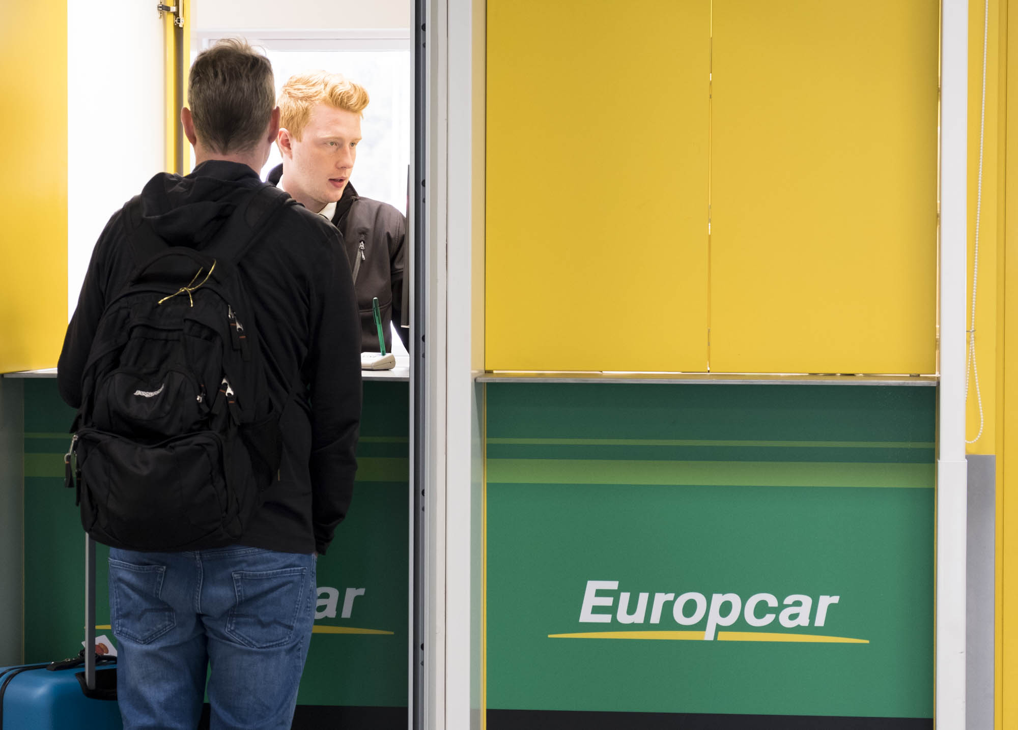 Traveler at an Akureyri Airport car rental counter with luggage.