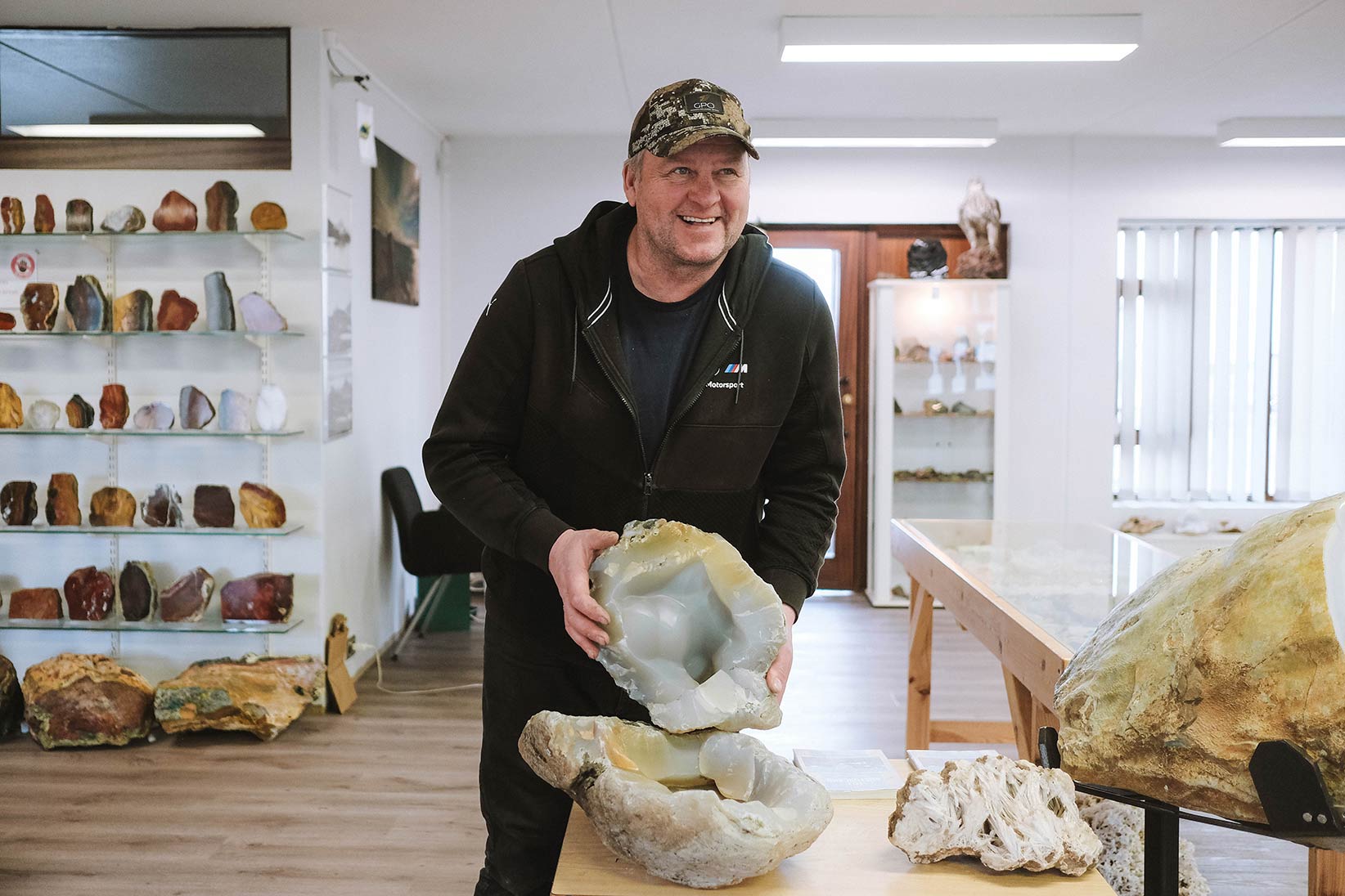 Audunn standing among large stones and display shelves at his Djúpivogur stone collection.