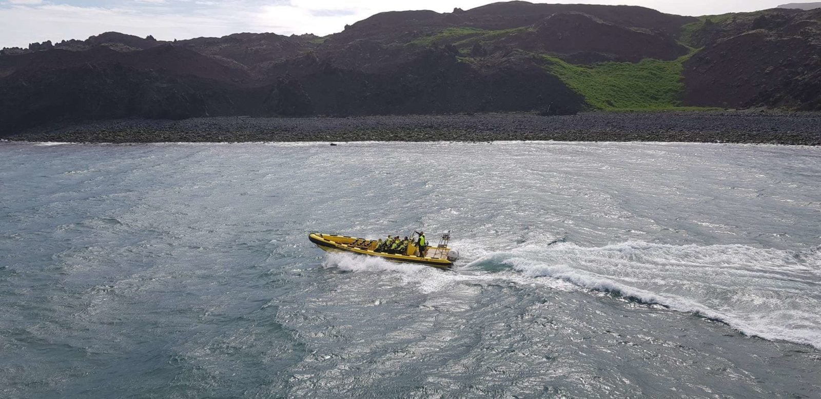 Bjarnarey Island rises steeply from the sea with dark cliffs and a thin band of green on top.