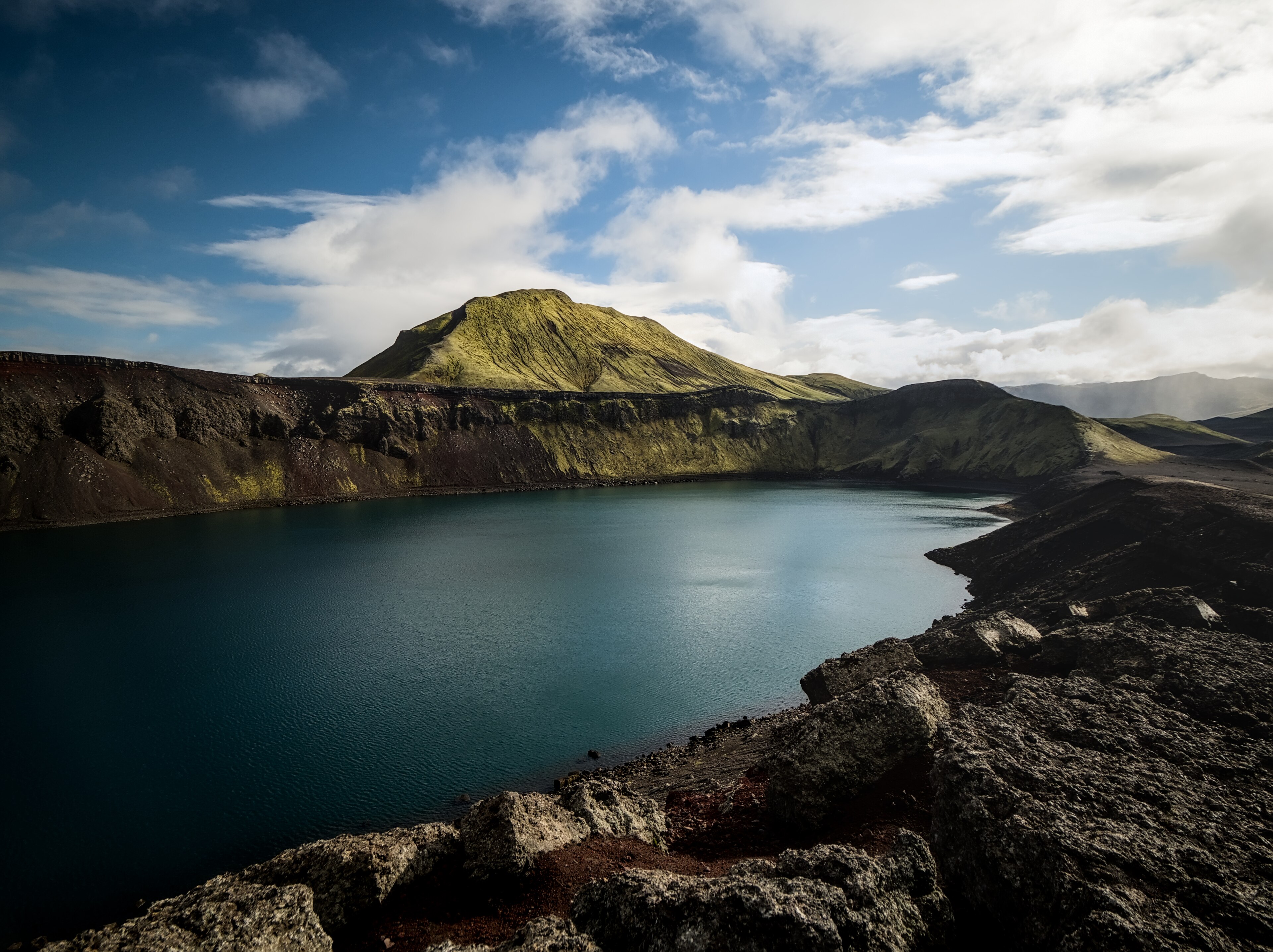 Bláhylur Hnausapollur crater lake below dark volcanic rim and green highland slopes.