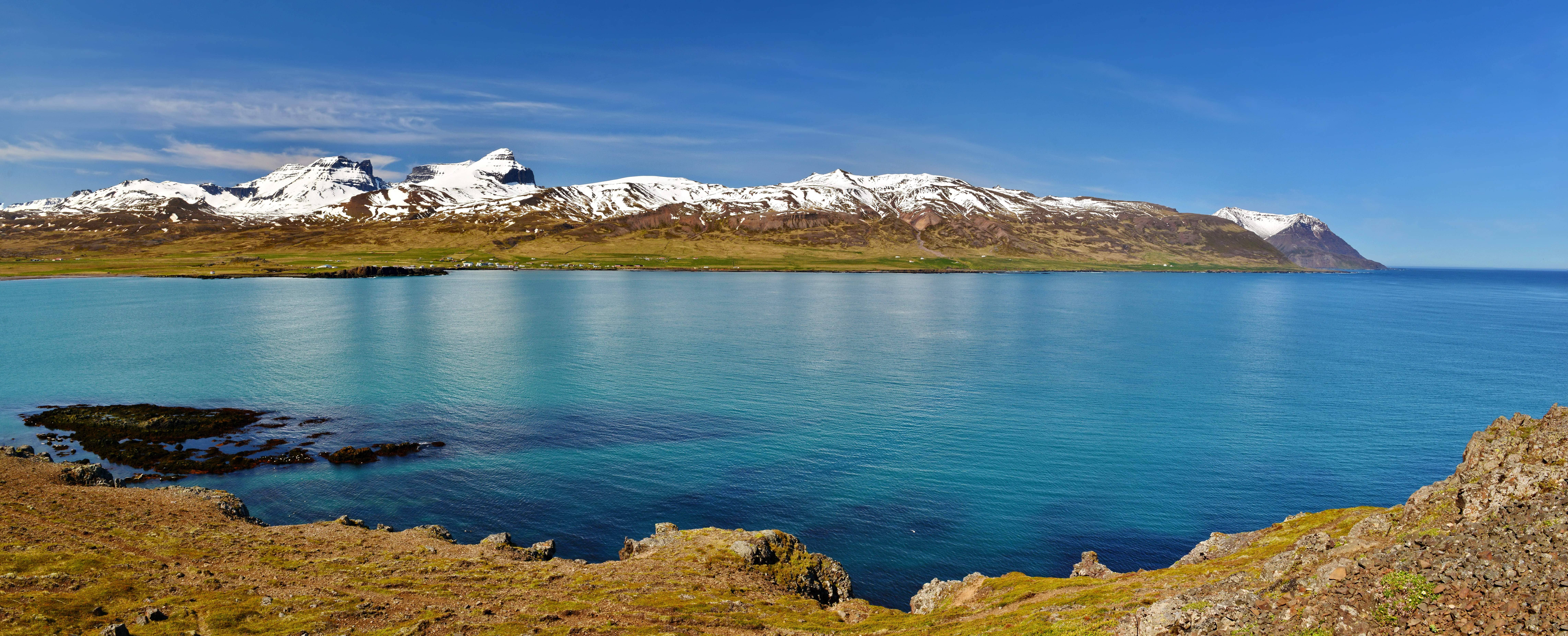 Wide coastal view near Borgarnes with turquoise water, cliffs, and snowy mountains.