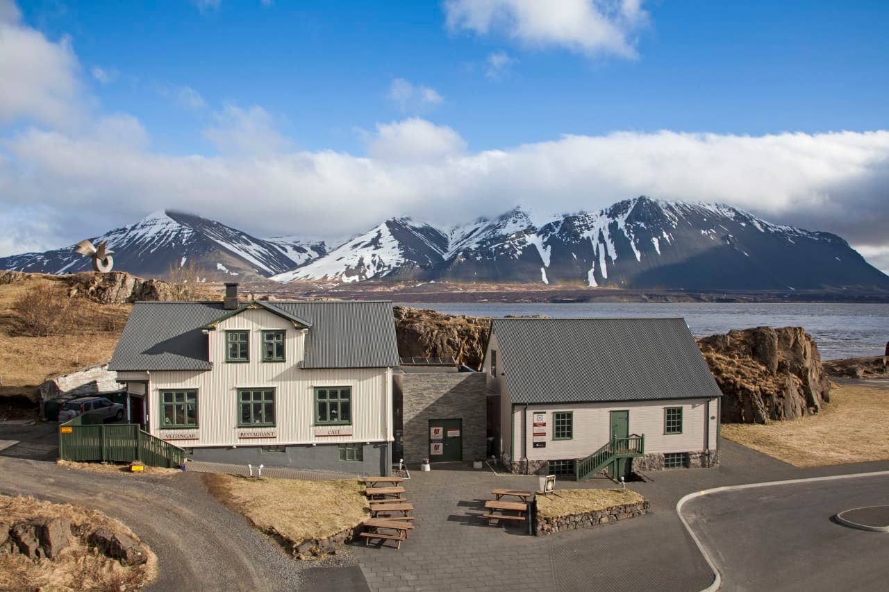 White buildings and picnic tables in Borgarnes with snow-capped mountains behind the town.