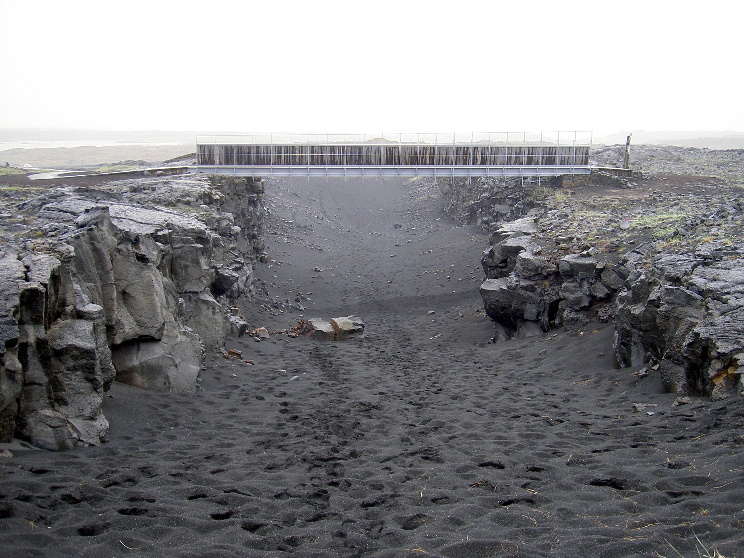Bridge Between Continents seen straight across the black-sand floor of the Álfagjá fissure.