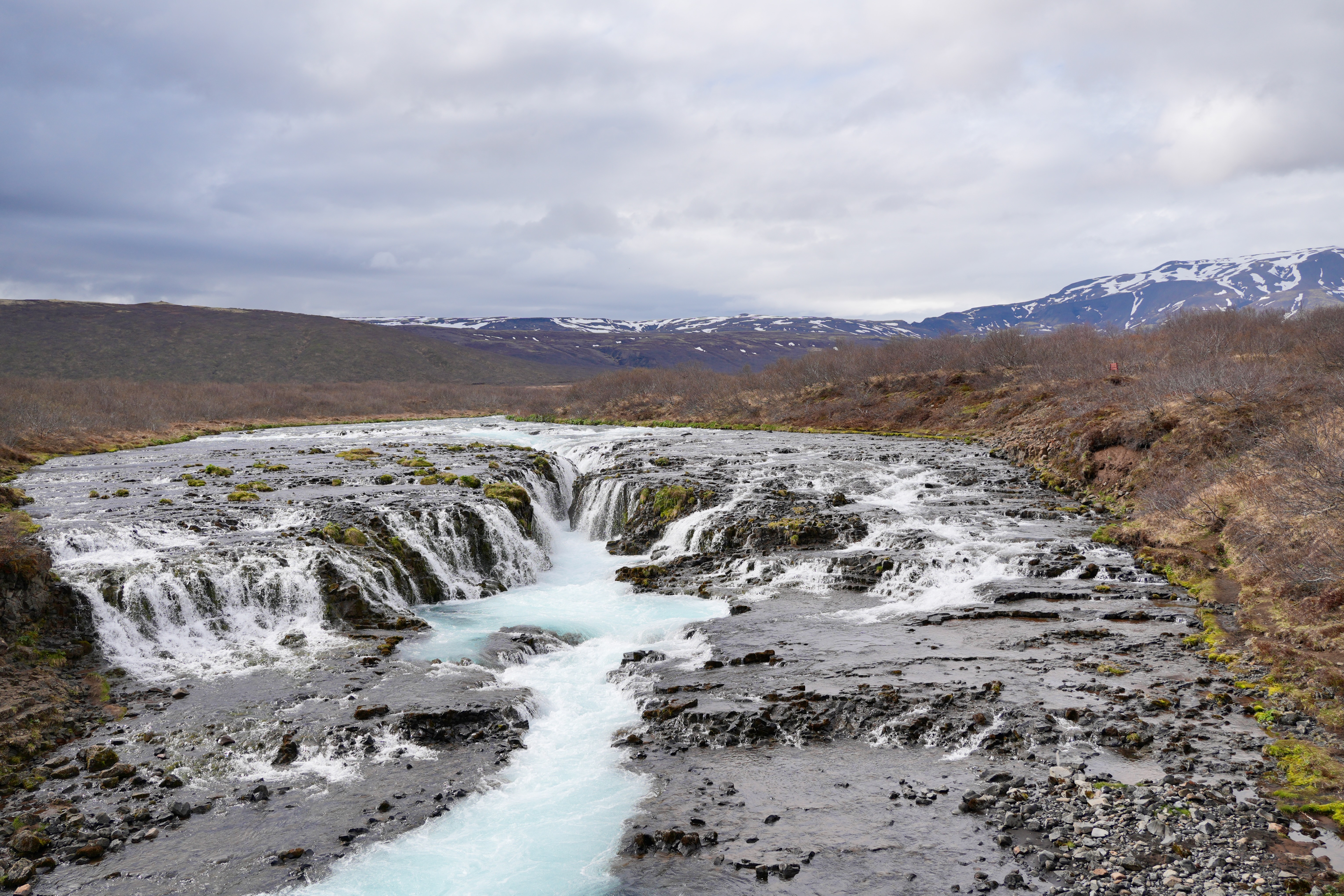 Wide view of Brúarfoss spreading across dark rock around the blue Brúará channel.