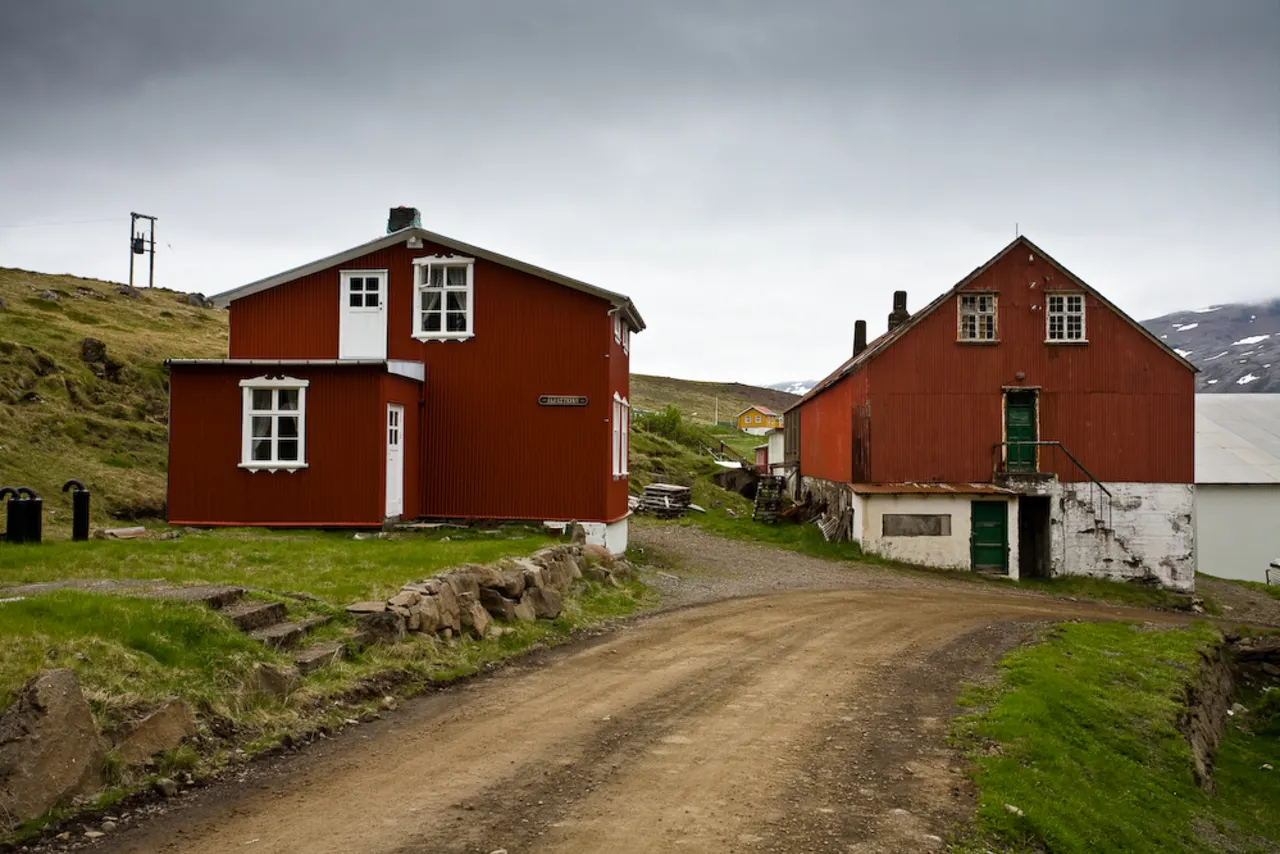 Village buildings in Djúpavík with Djúpavíkurfoss dropping down the cliff behind them.