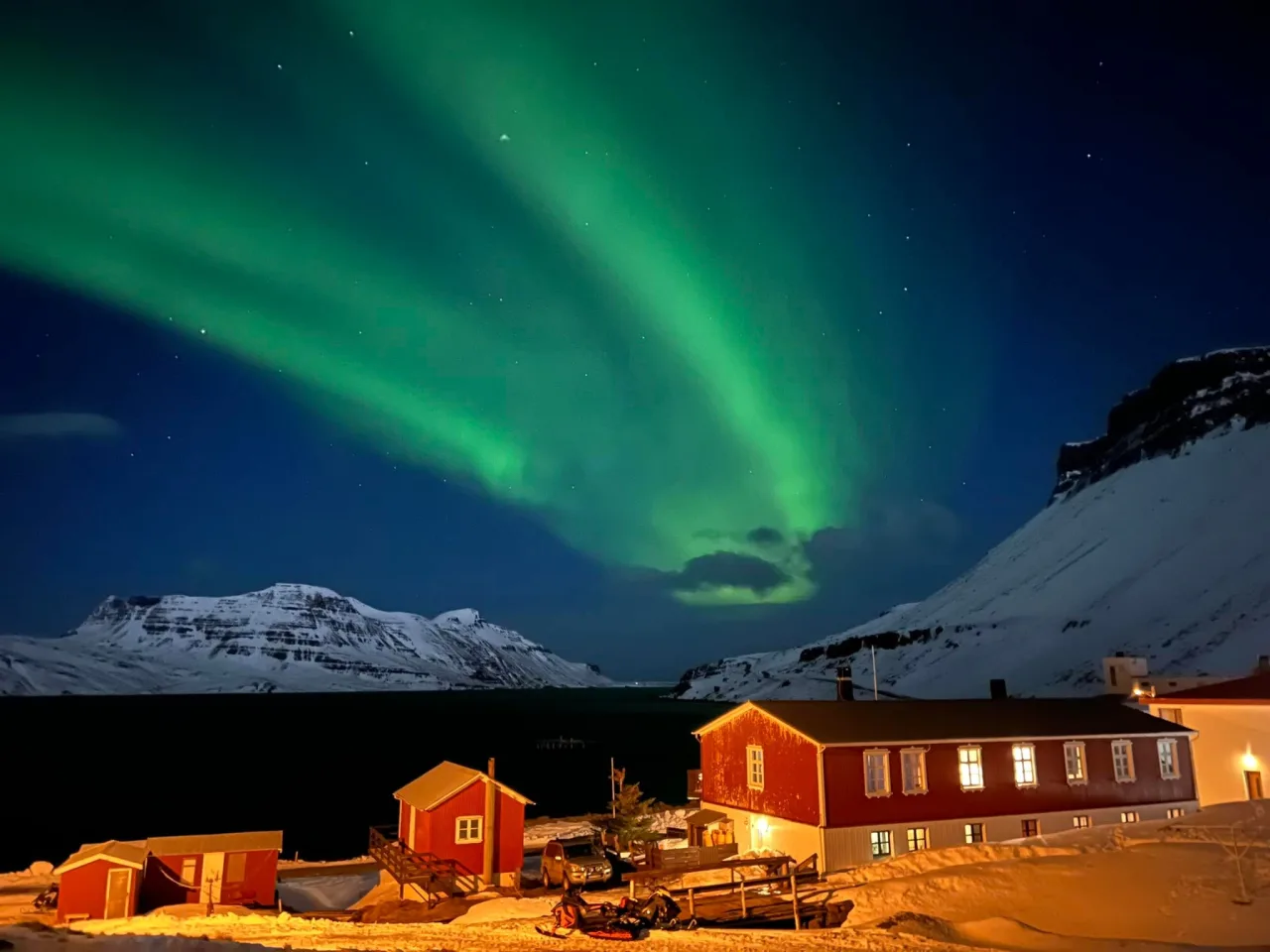 Hotel Djúpavík under northern lights beside the fjord at night.