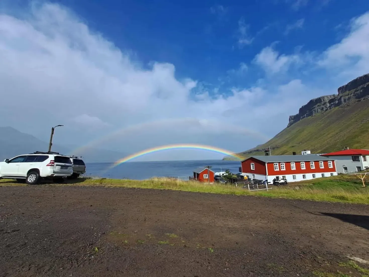 Hotel Djúpavík and nearby red buildings under a rainbow beside Reykjarfjörður.