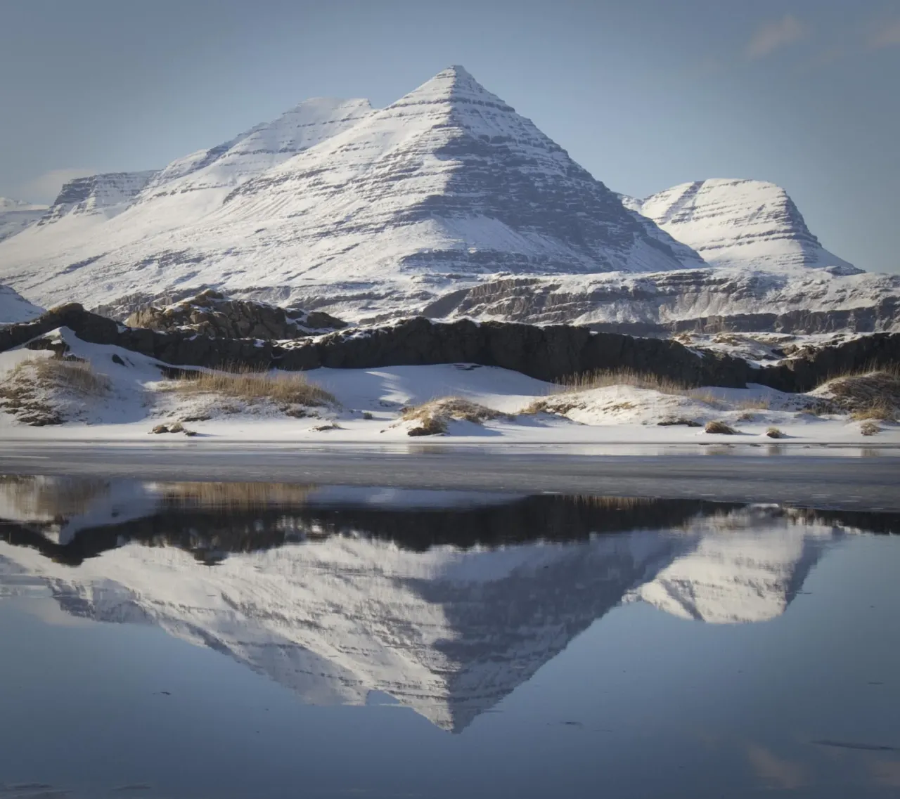 Snow-covered Búlandstindur mountain reflected in still water near Djúpivogur.