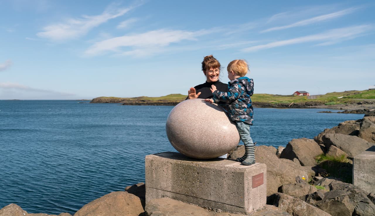 Visitor and child beside one of the Eggin í Gleðivík sculptures on the Djúpivogur waterfront.
