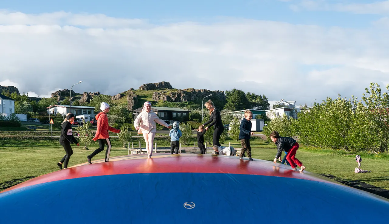 Children playing in a green public area in Djúpivogur with houses and rocky hills behind.
