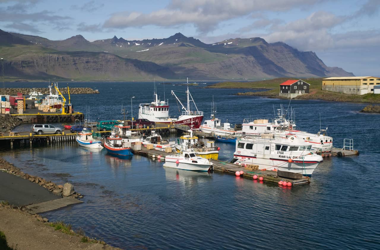 Fishing boats in Djúpivogur harbor with dark mountains across the water.