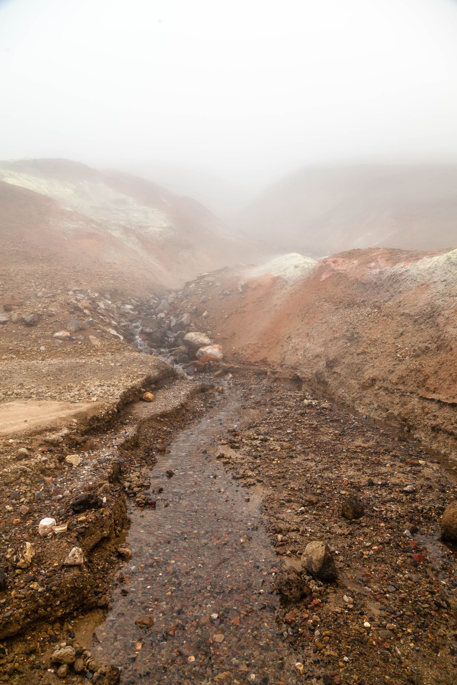 Muddy stream channel and loose volcanic ground in misty Drekagil terrain.