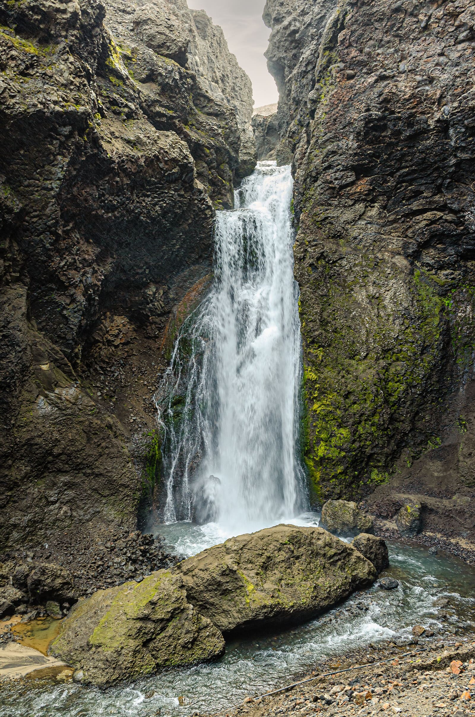 Waterfall dropping between steep dark rock walls inside Drekagil gorge.
