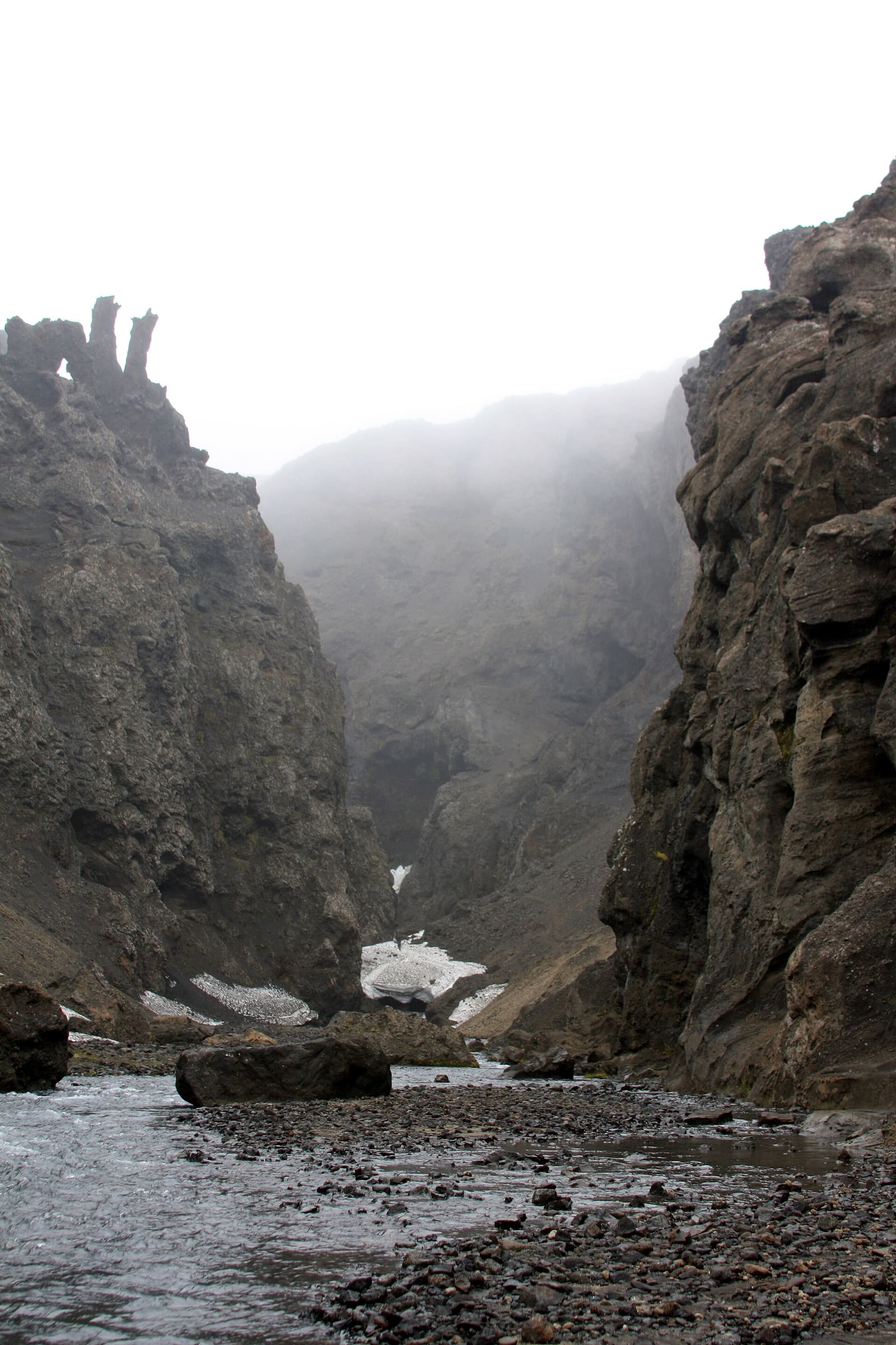 Lingering snow below the dark cliffs and stream inside Drekagil.