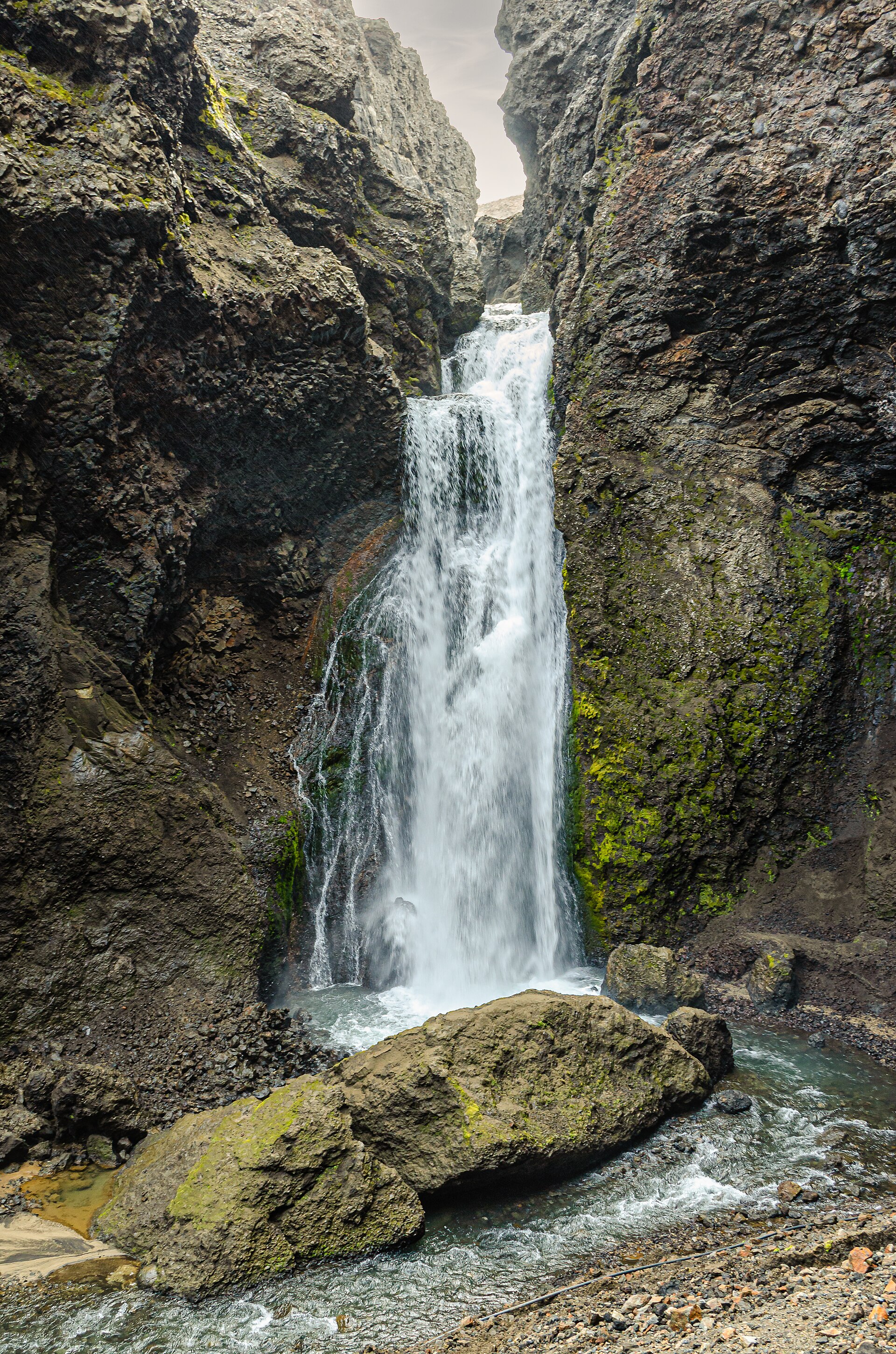Waterfall dropping between steep dark rock walls inside Drekagil gorge.