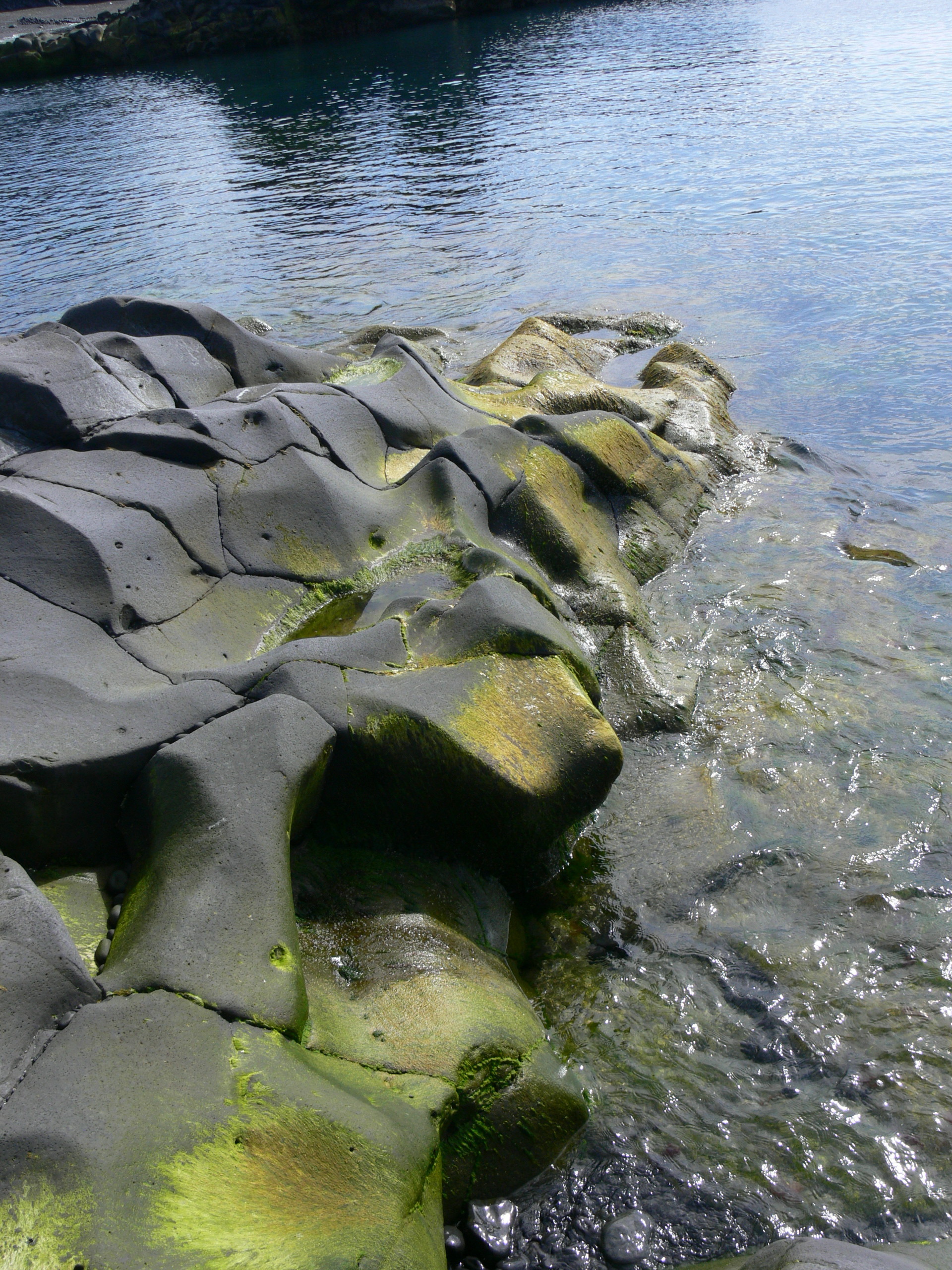 Rounded dark shoreline rocks beside clear water at Dritvík Cove.