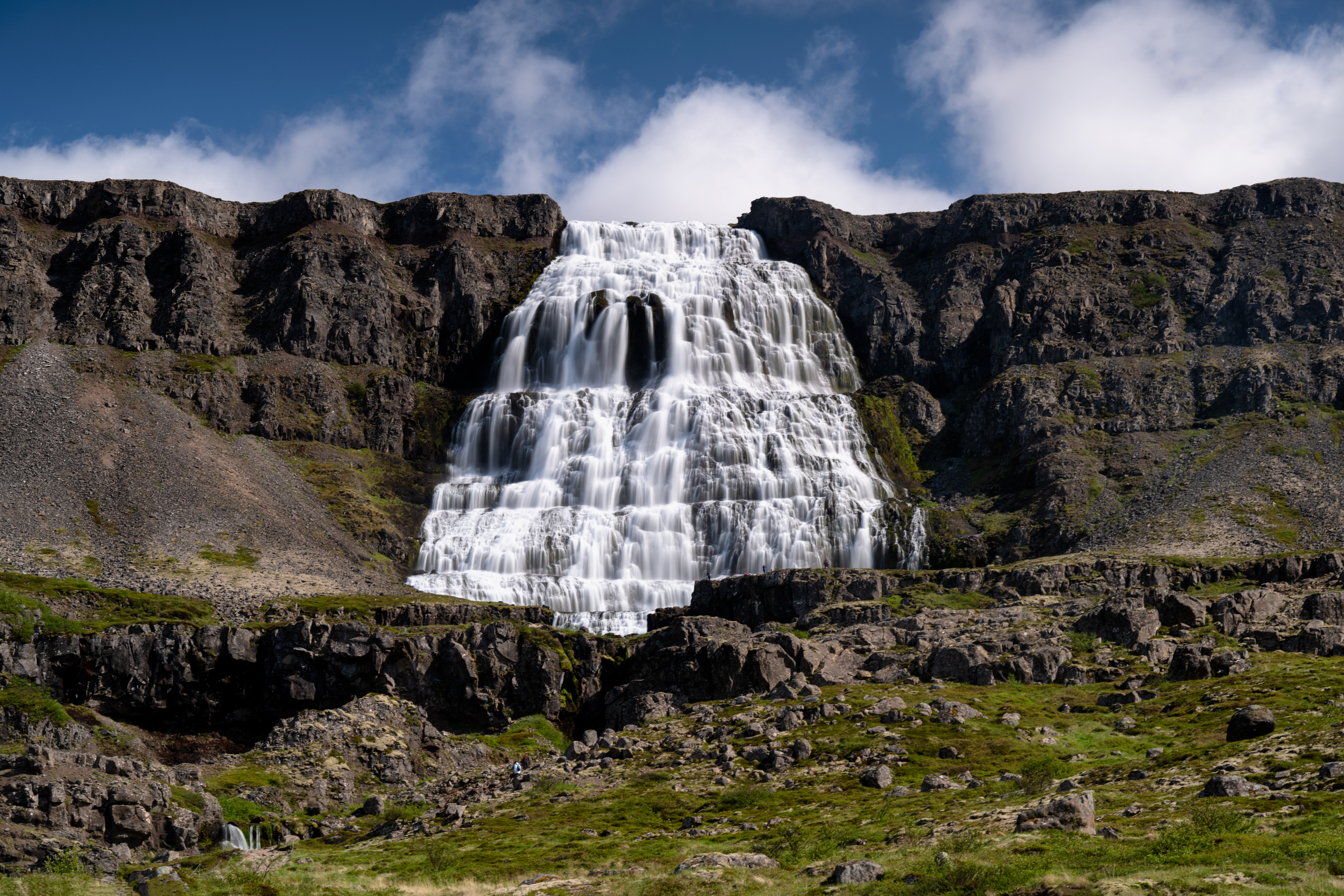 Dynjandi waterfall spreading across a stepped rock cliff below blue sky.