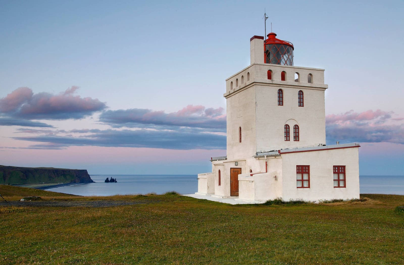 Dyrhólaey Lighthouse above the South Coast with Reynisdrangar and Reynisfjara in the distance.