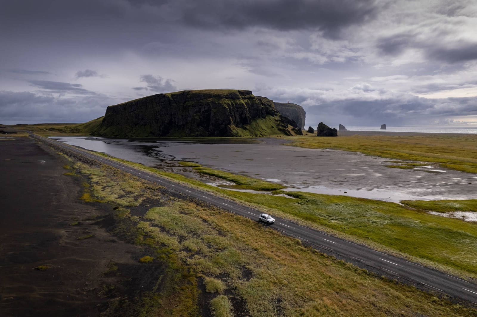 White car on the South Coast road below Dyrhólaey, wetlands, cliffs, and Reynisdrangar