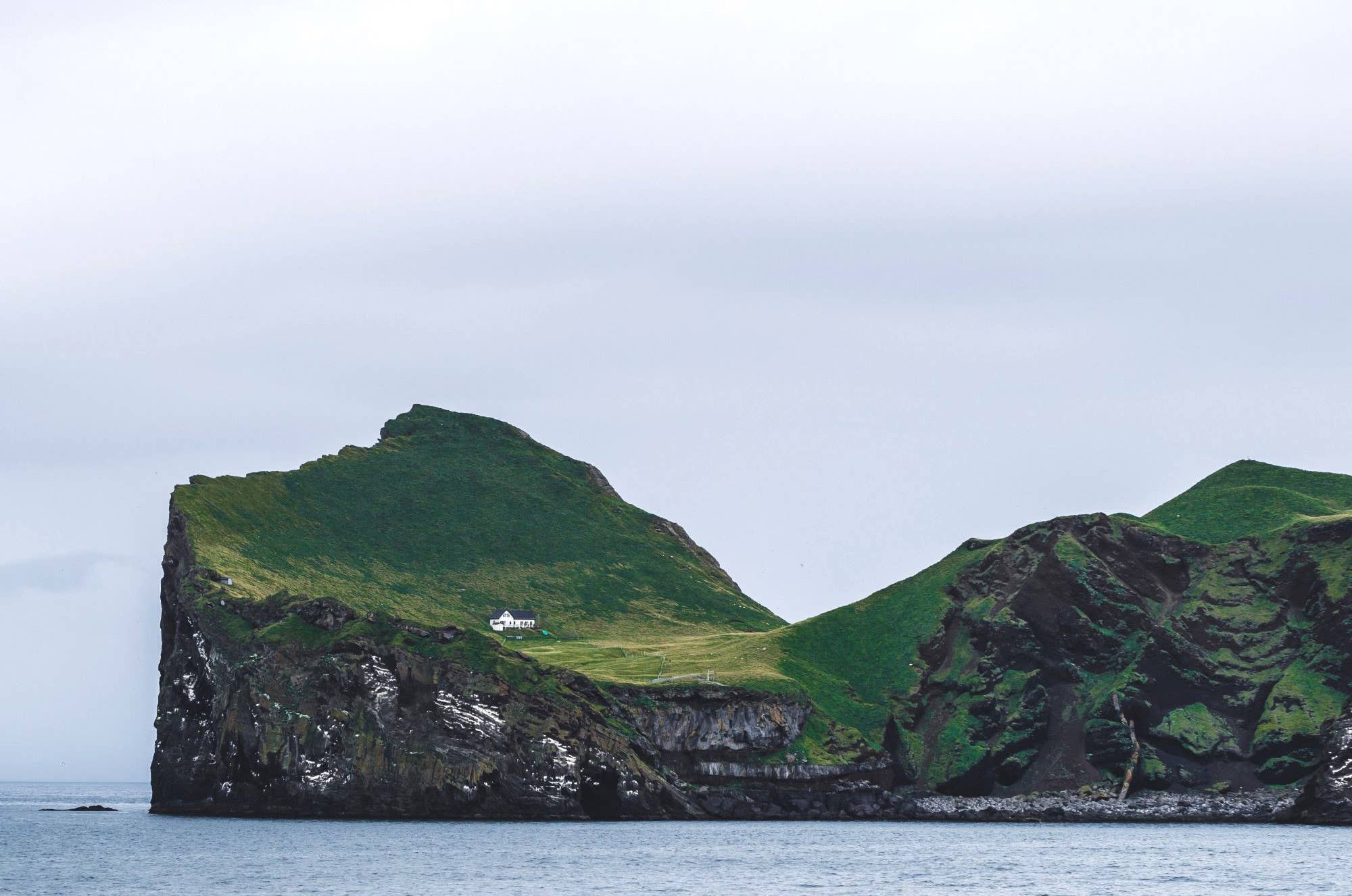 Steep green slopes and cliffs on Ellidaey Island in the Westman Islands.
