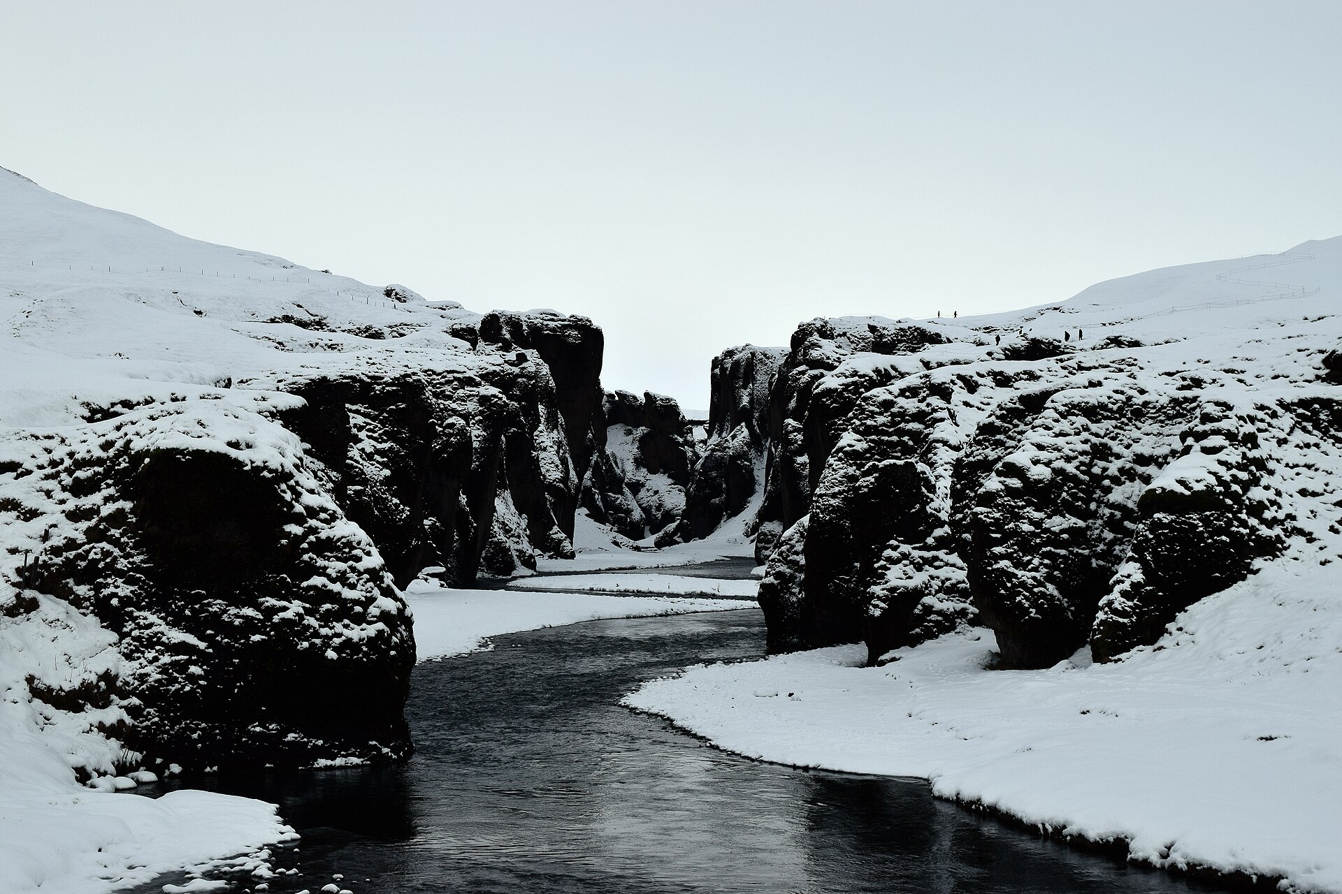 Snow-covered walls and a dark river inside Fjaðrárgljúfur during winter conditions.