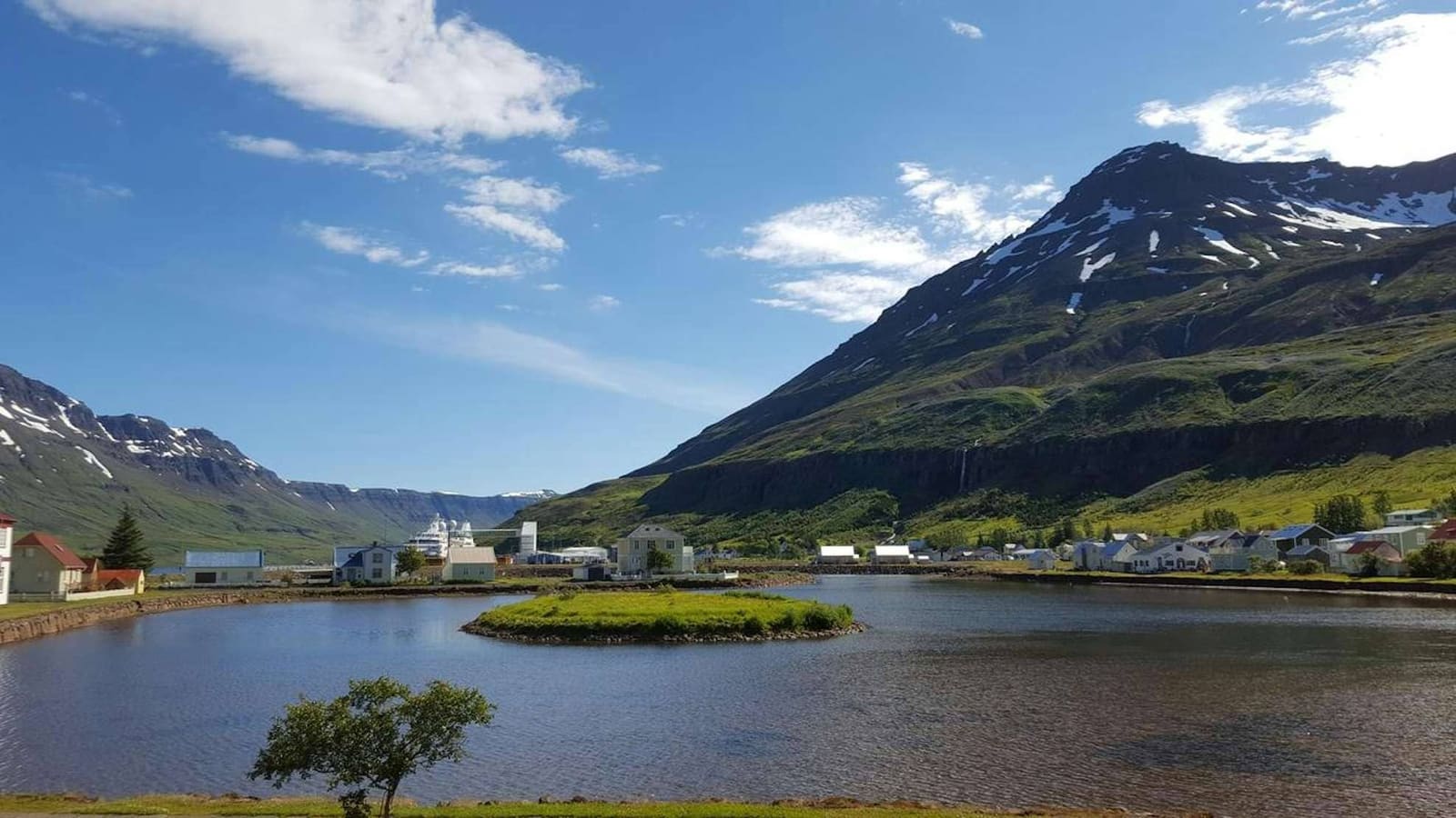 Fjardara Lake reflecting Seydisfjordur buildings and Eastfjords mountains.