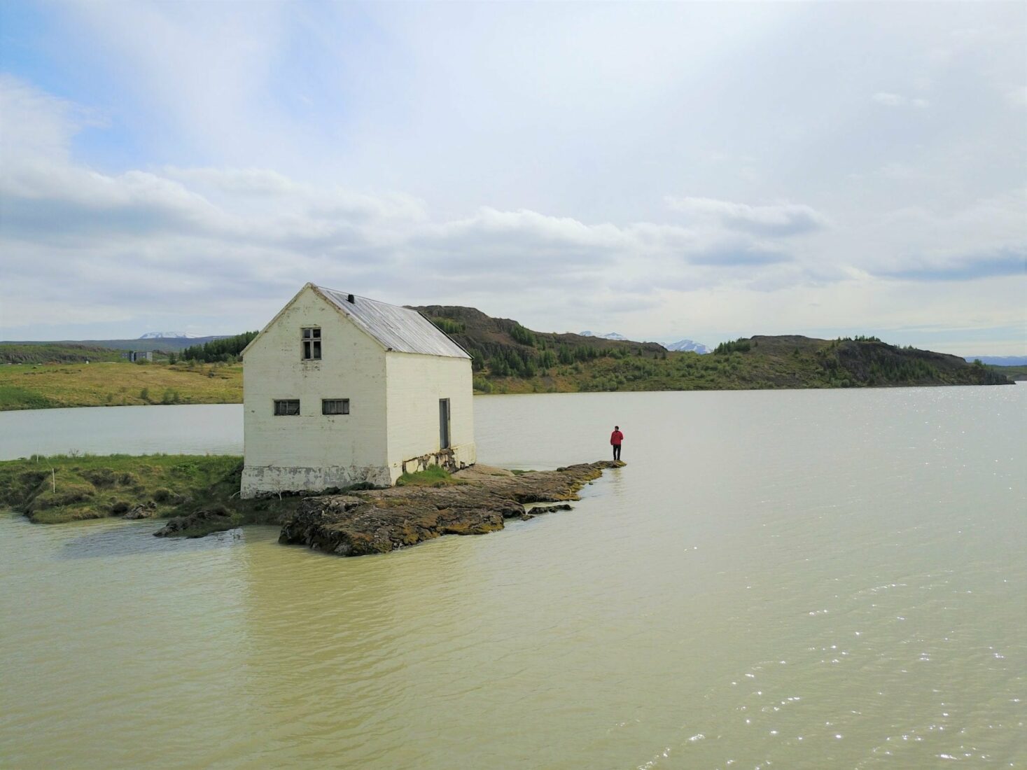An old house by Lagarfljót with open water and East Iceland hills in the Fljótsdalshérað area.