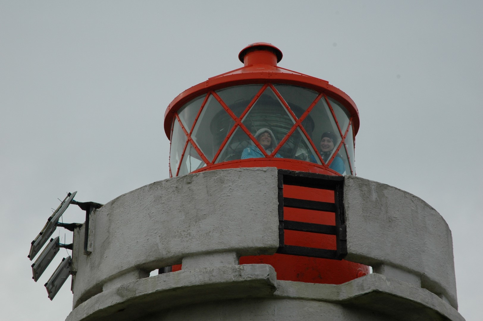 Close view of the red lantern and white concrete top of Fontur lighthouse in grey weather.