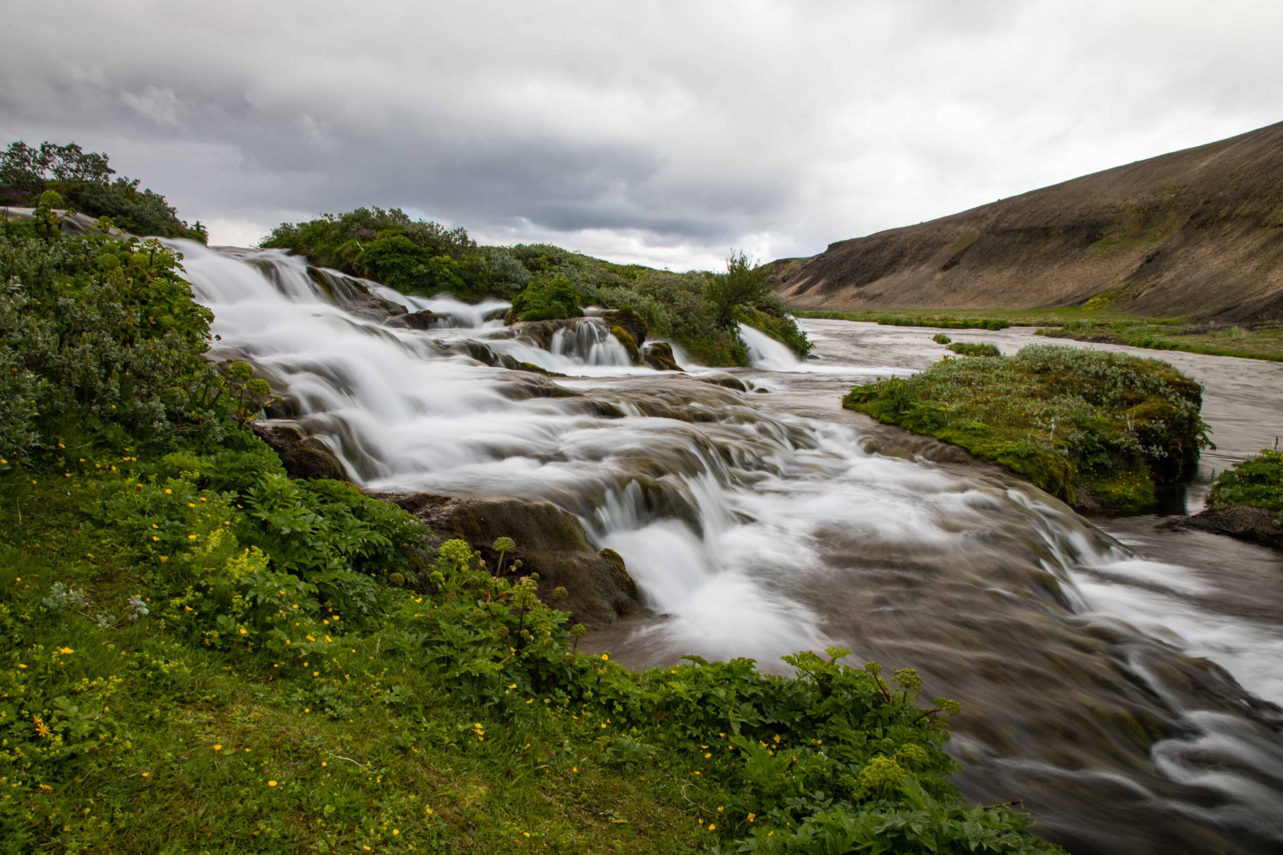 Fossabrekkur waterfalls spread across a green slope in the volcanic landscape near Hekla.
