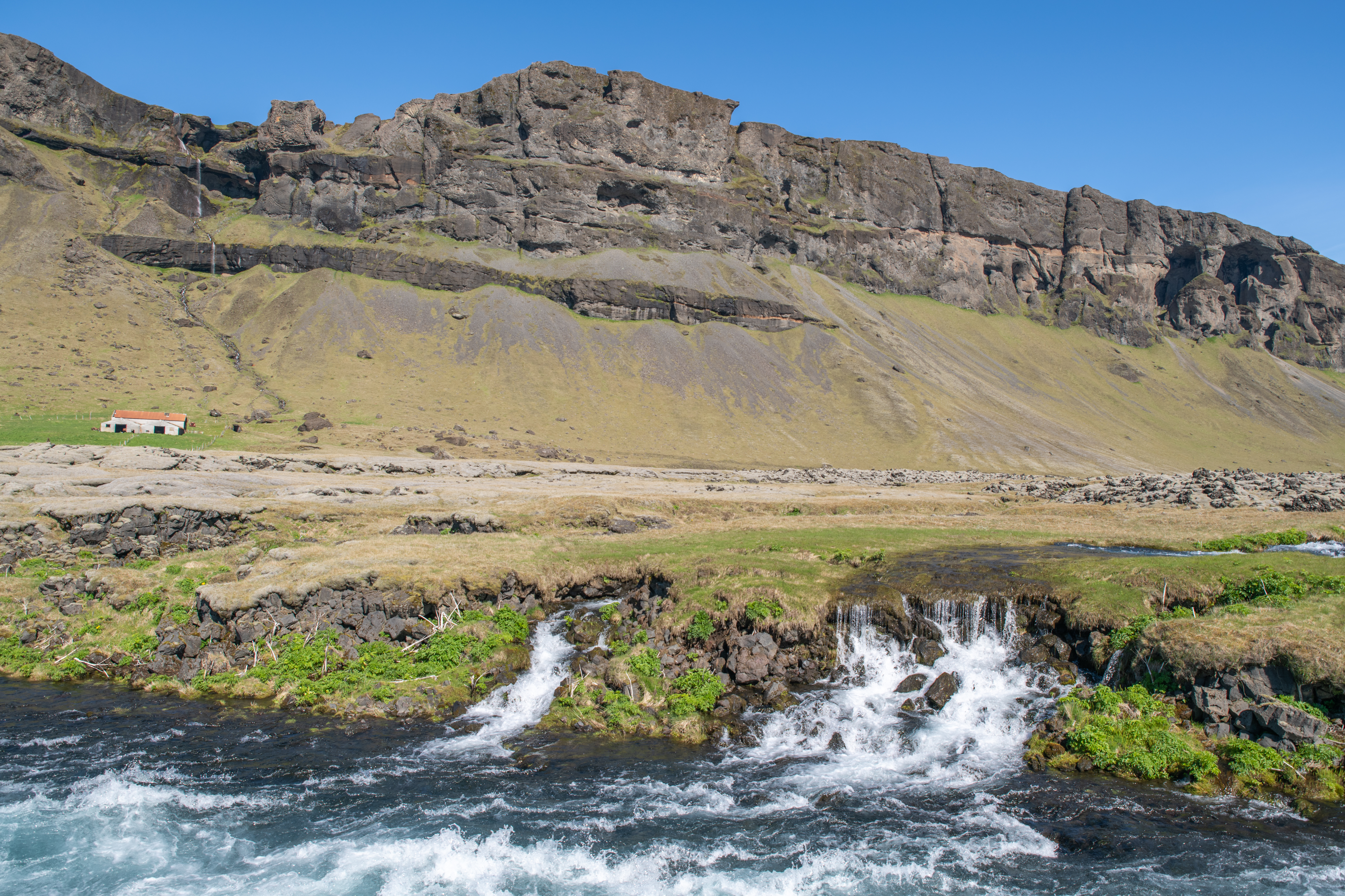 Low Fossálar cascades running through dark rock below cliffs in South Iceland.