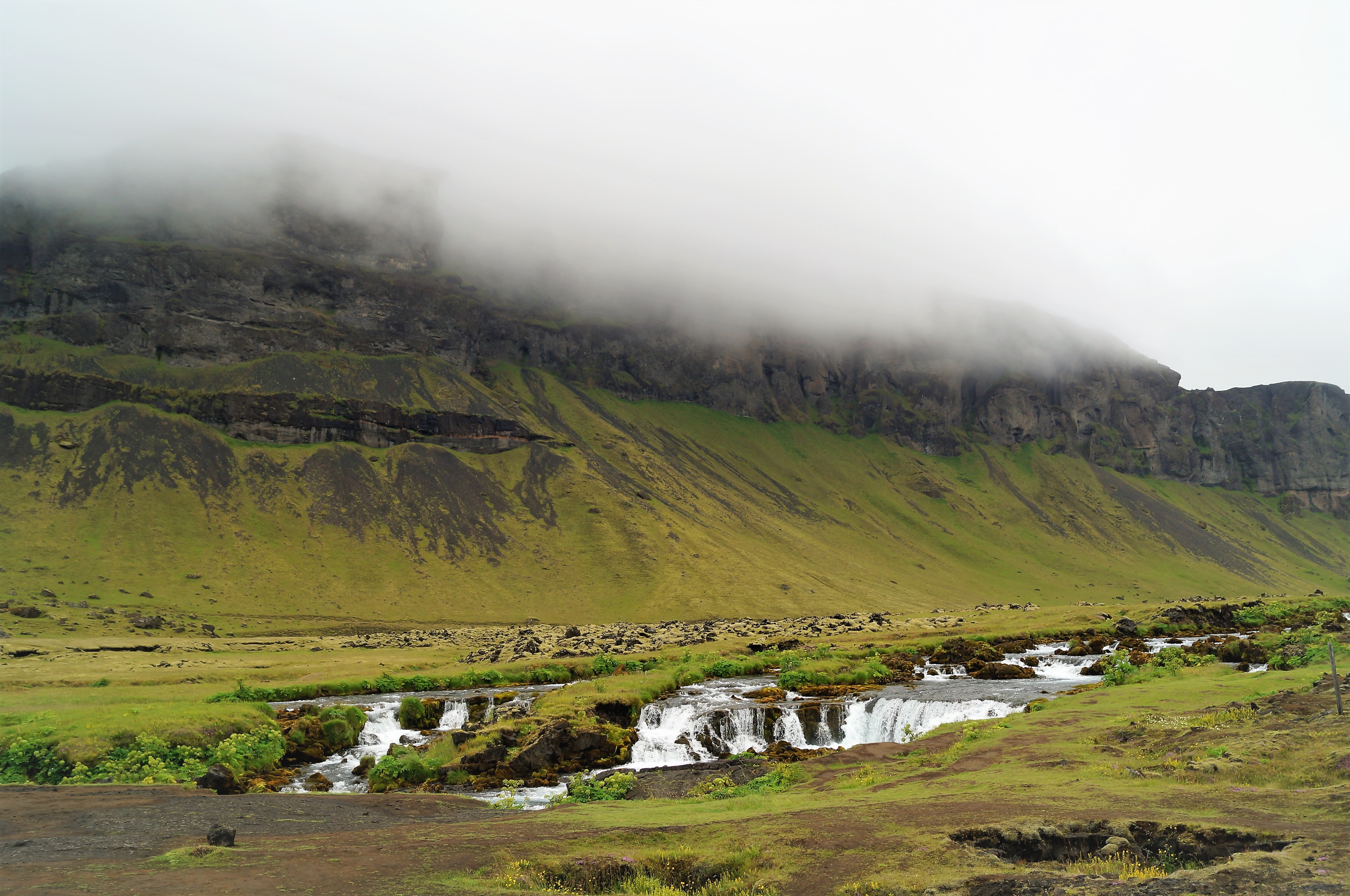 Fossálar river and low waterfalls below green South Iceland slopes.