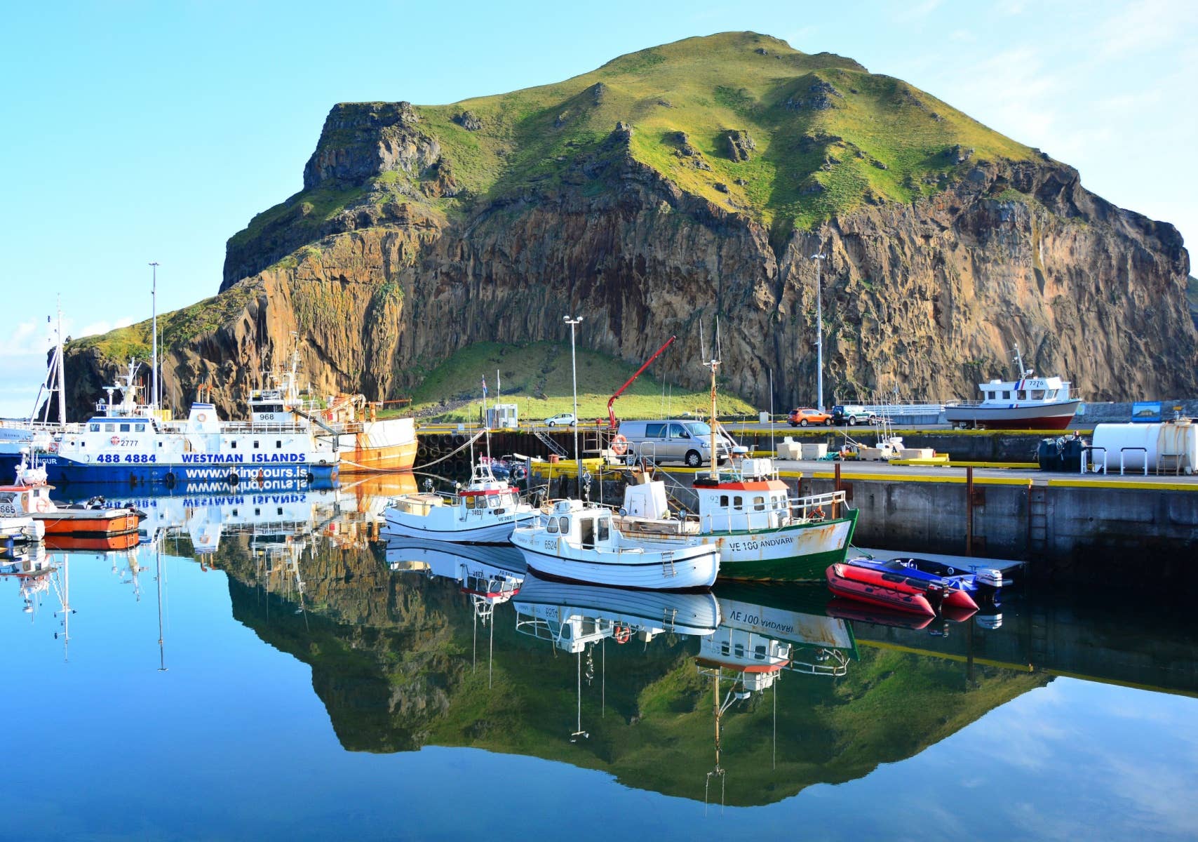 Heimaey harbor with fishing boats below steep Westman Islands cliffs.