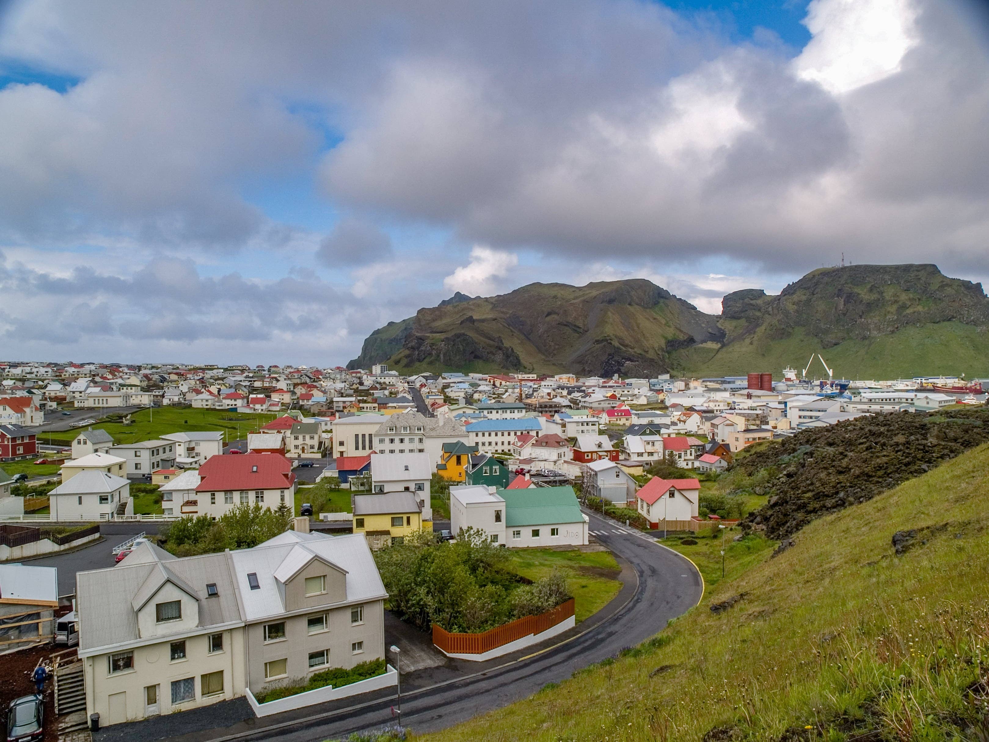 Colorful houses in Heimaey town with volcanic cliffs rising behind them.