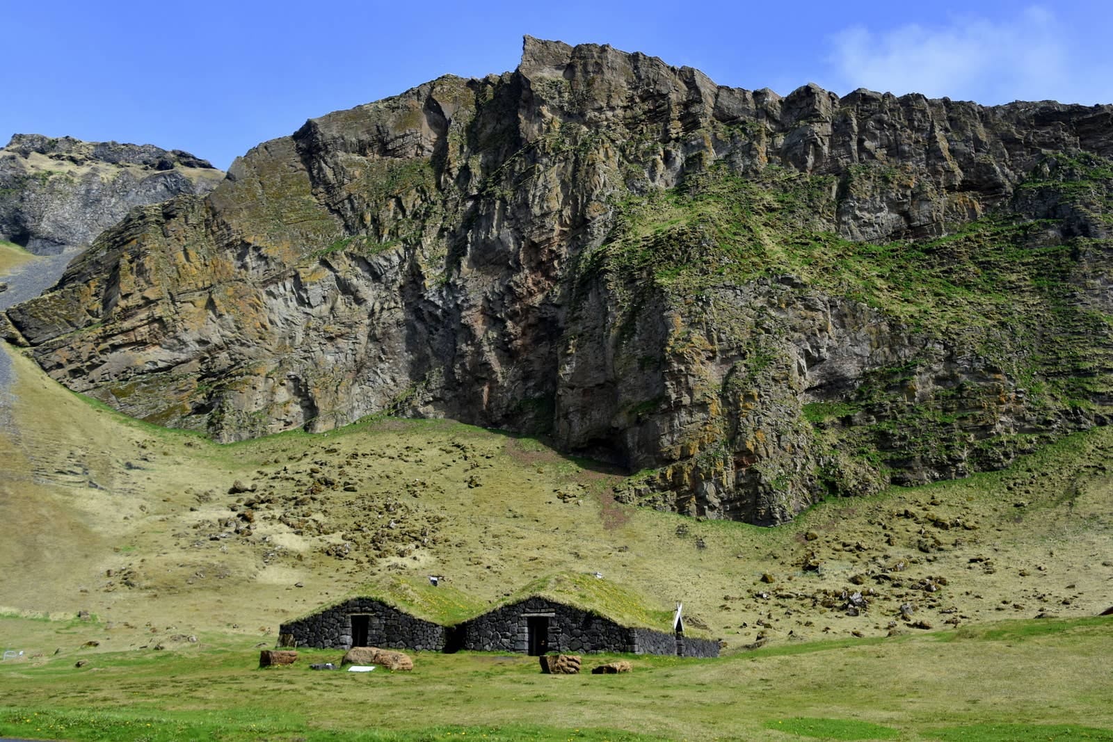 Turf and stone house in green Herjolfsdalur Valley below Heimaey cliffs.