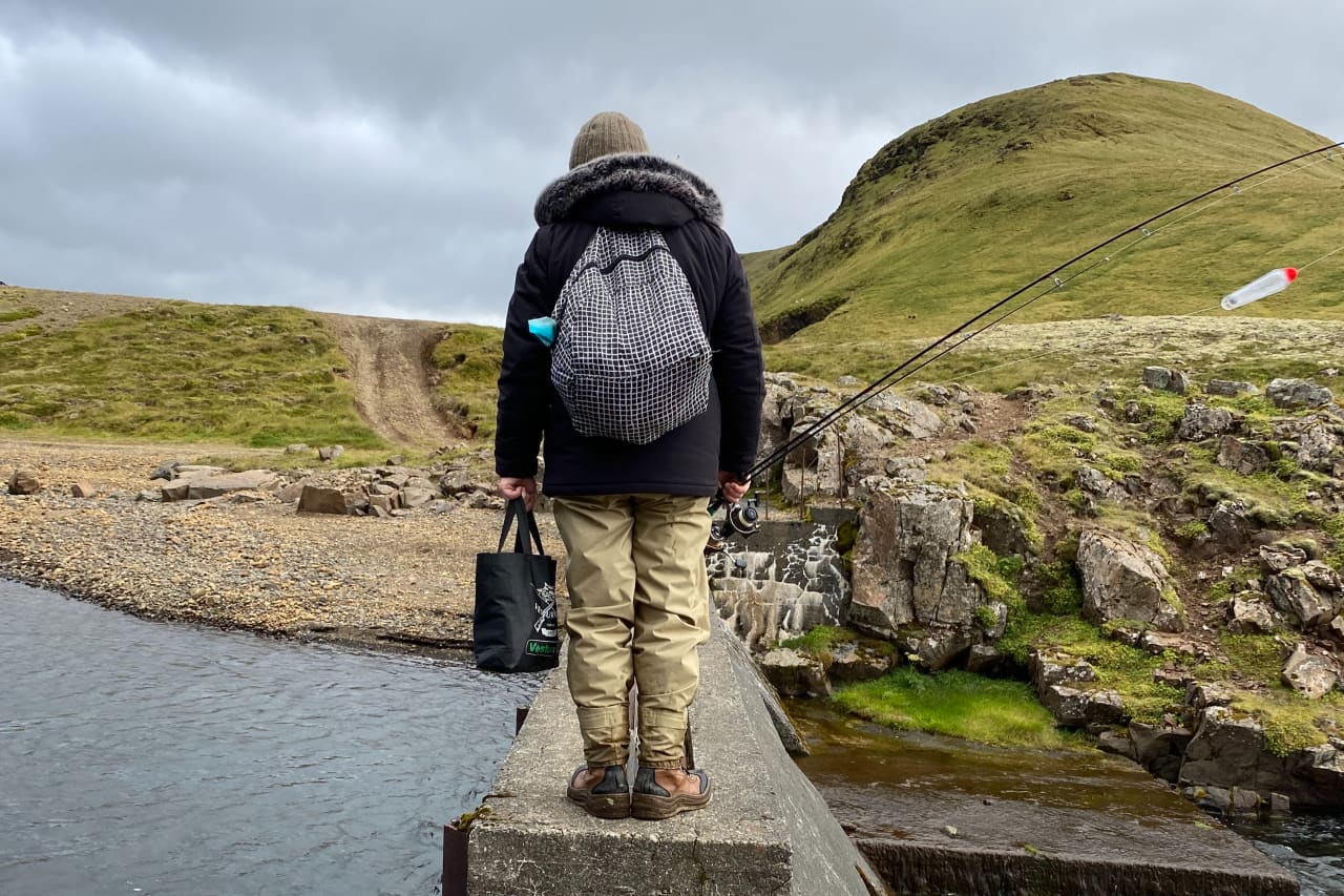 Angler carrying a fishing rod beside water near Hlíðarvatn