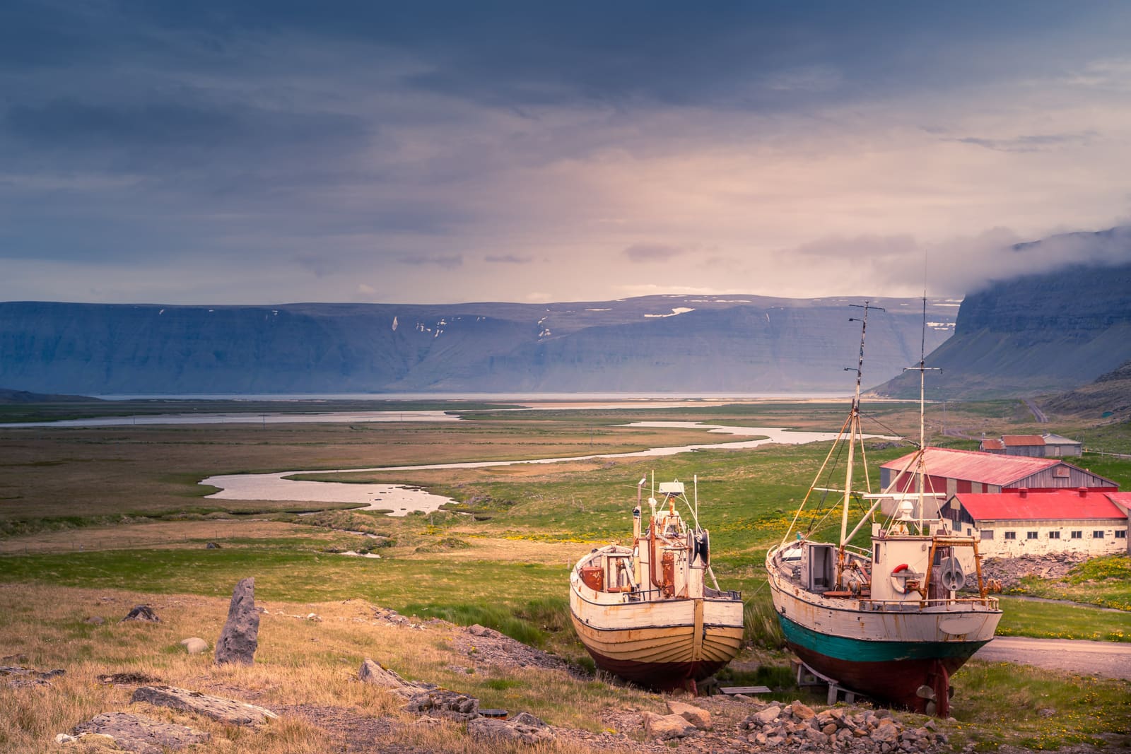 Old boats and red-roofed buildings overlooking a fjord near Hnjótur Museum.