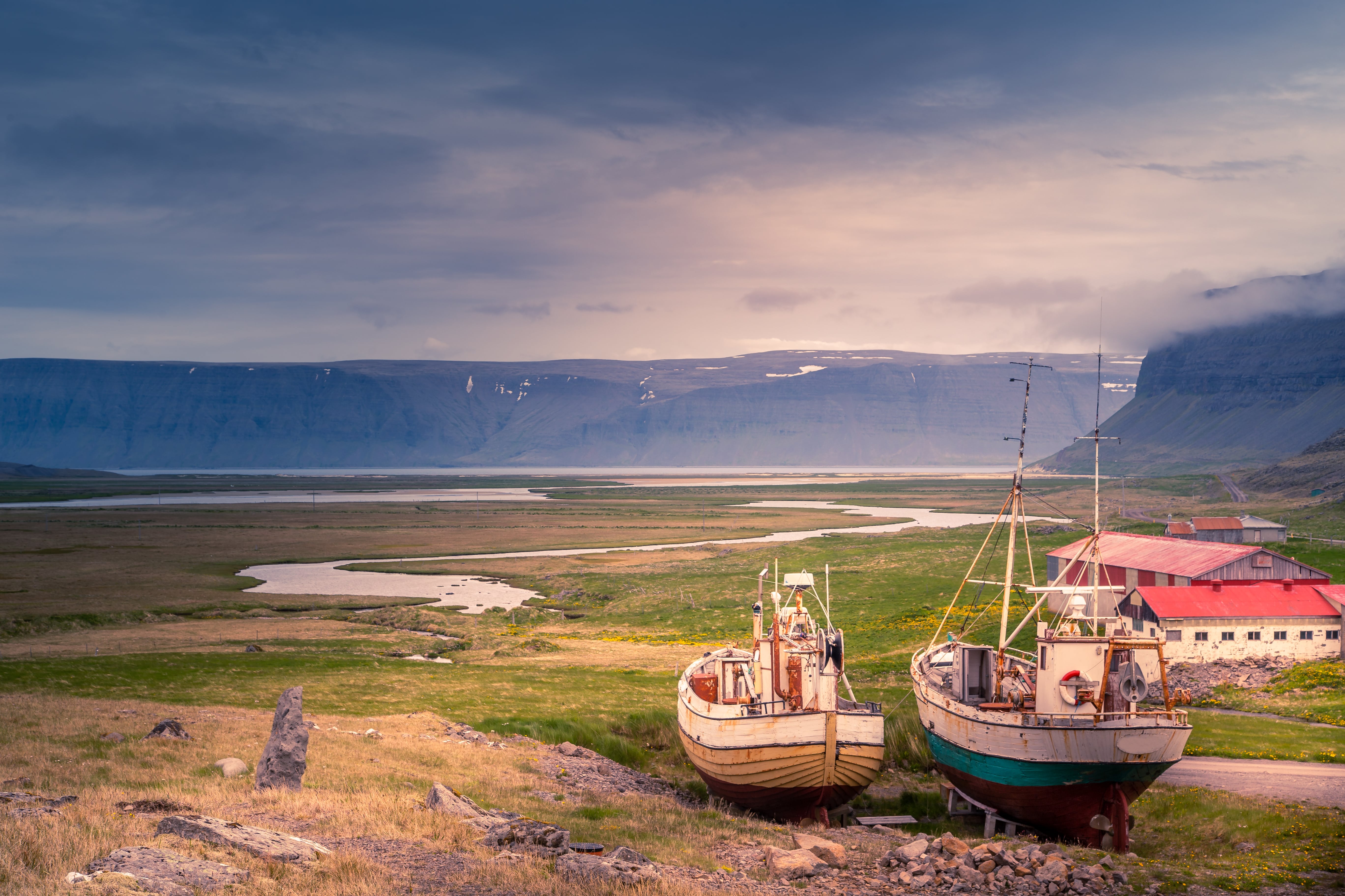Old boats and red-roofed buildings overlooking a fjord near Hnjótur Museum.