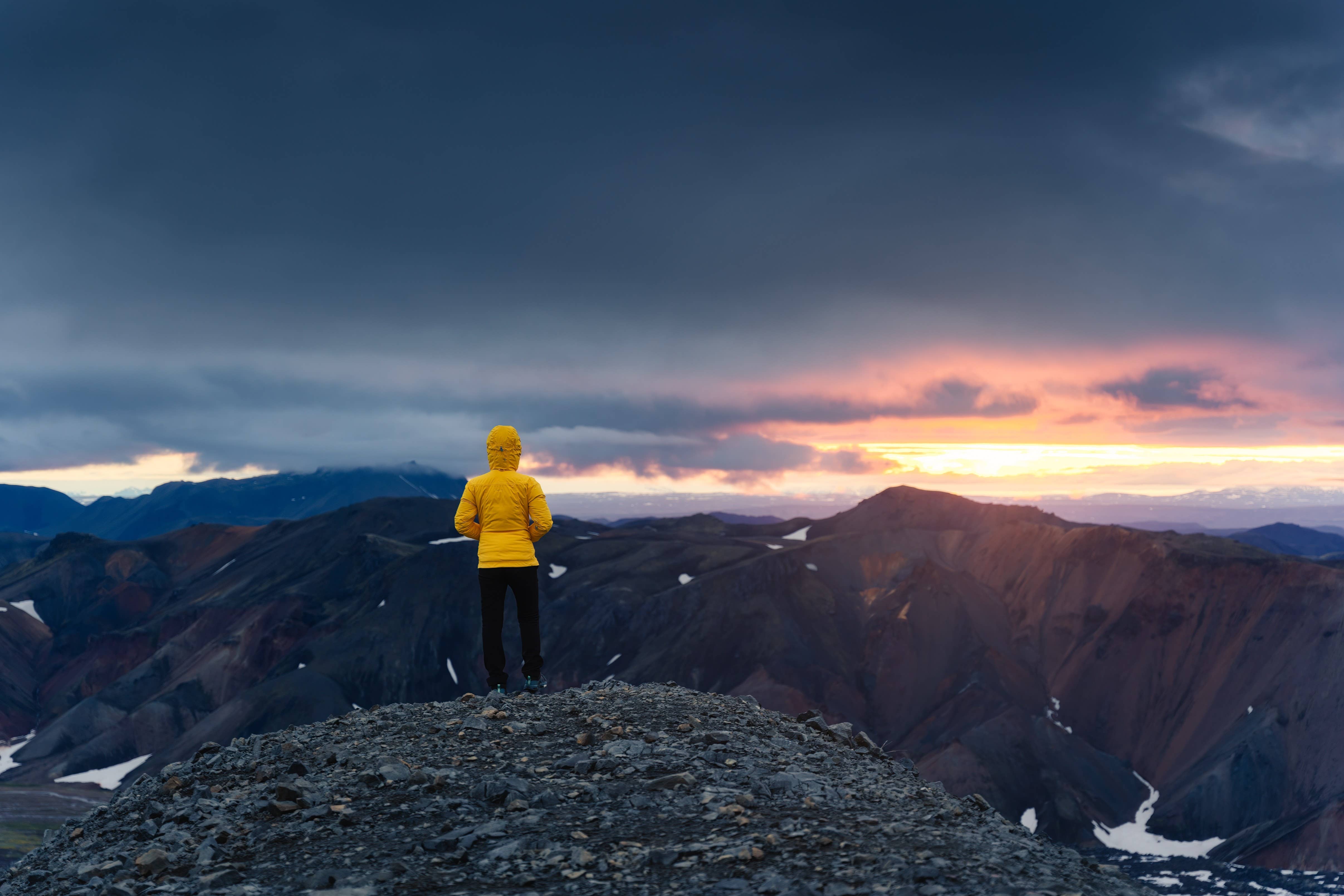 Hiker in a yellow jacket looking across Hrafntinnusker highland terrain in low light.