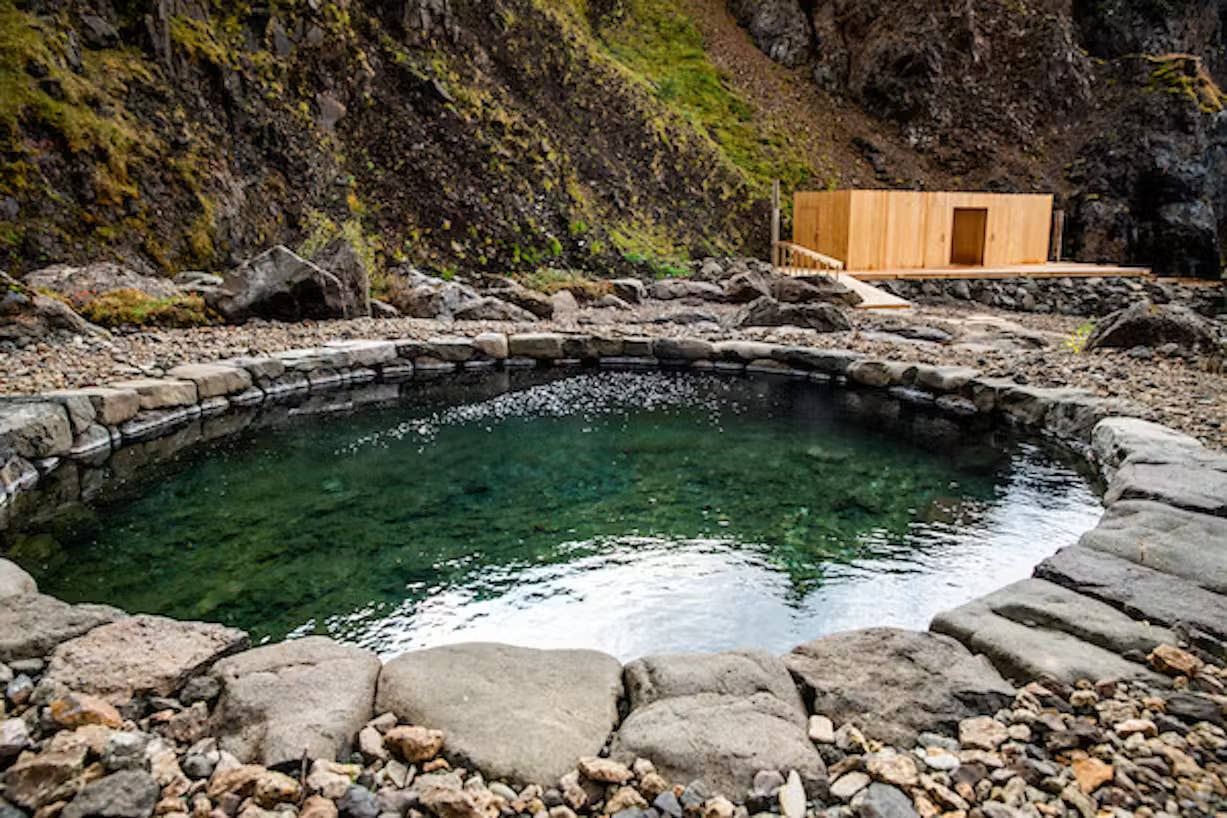 Stone-edged geothermal pool at Húsafell Canyon Baths with canyon rock behind it.